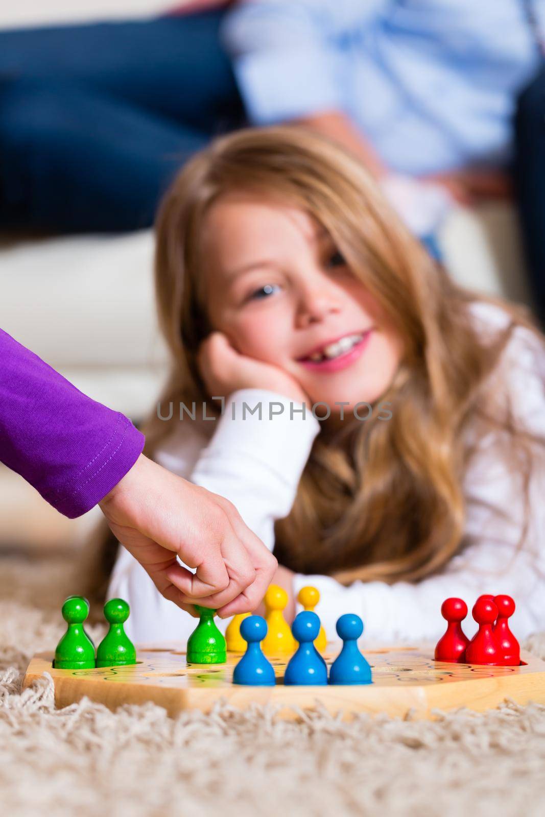 Family playing board game ludo at home on the floor, focus on the arm in front