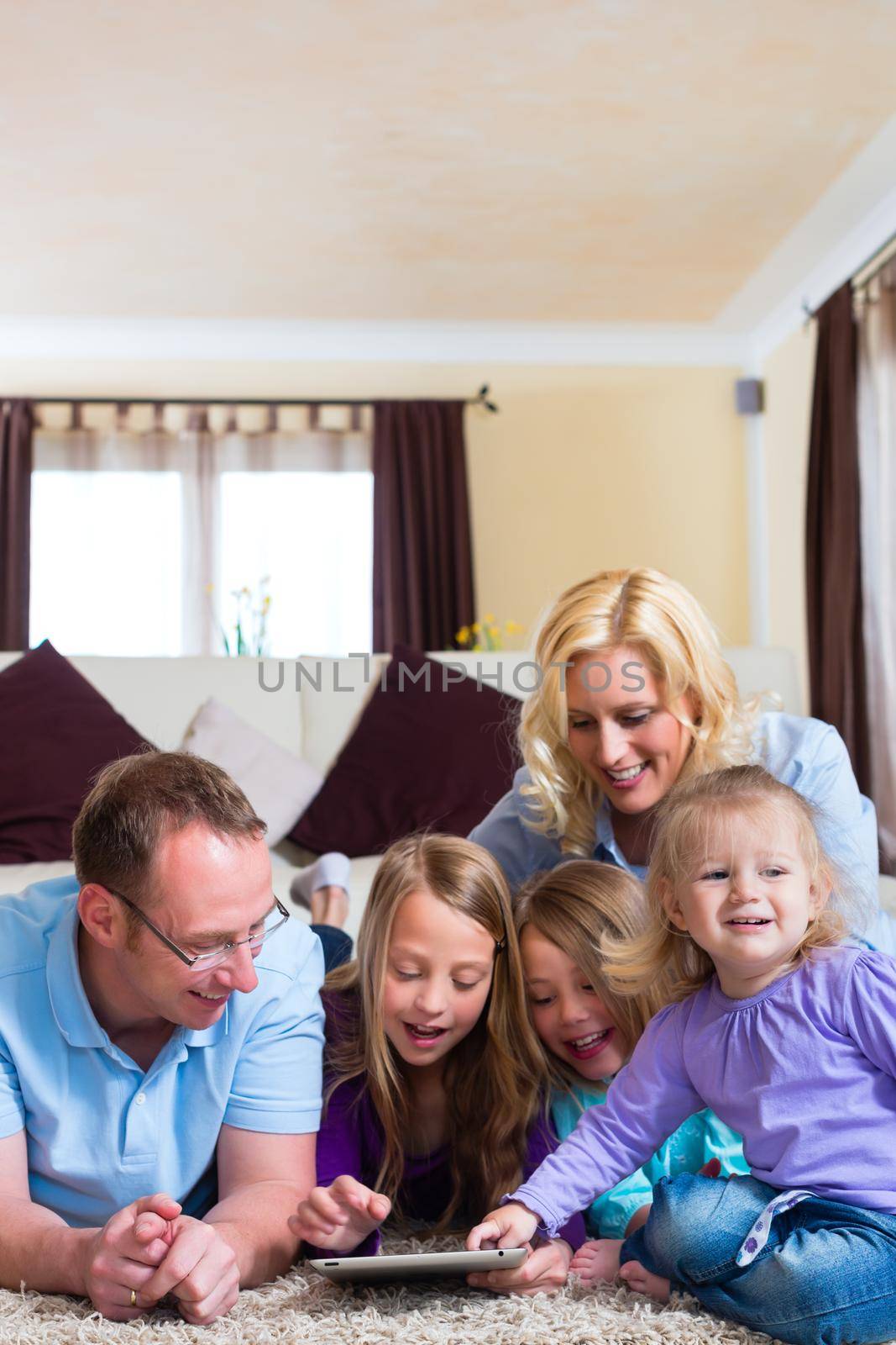 Family - mother, father, daughters - playing with tablet computer lying on the floor at home