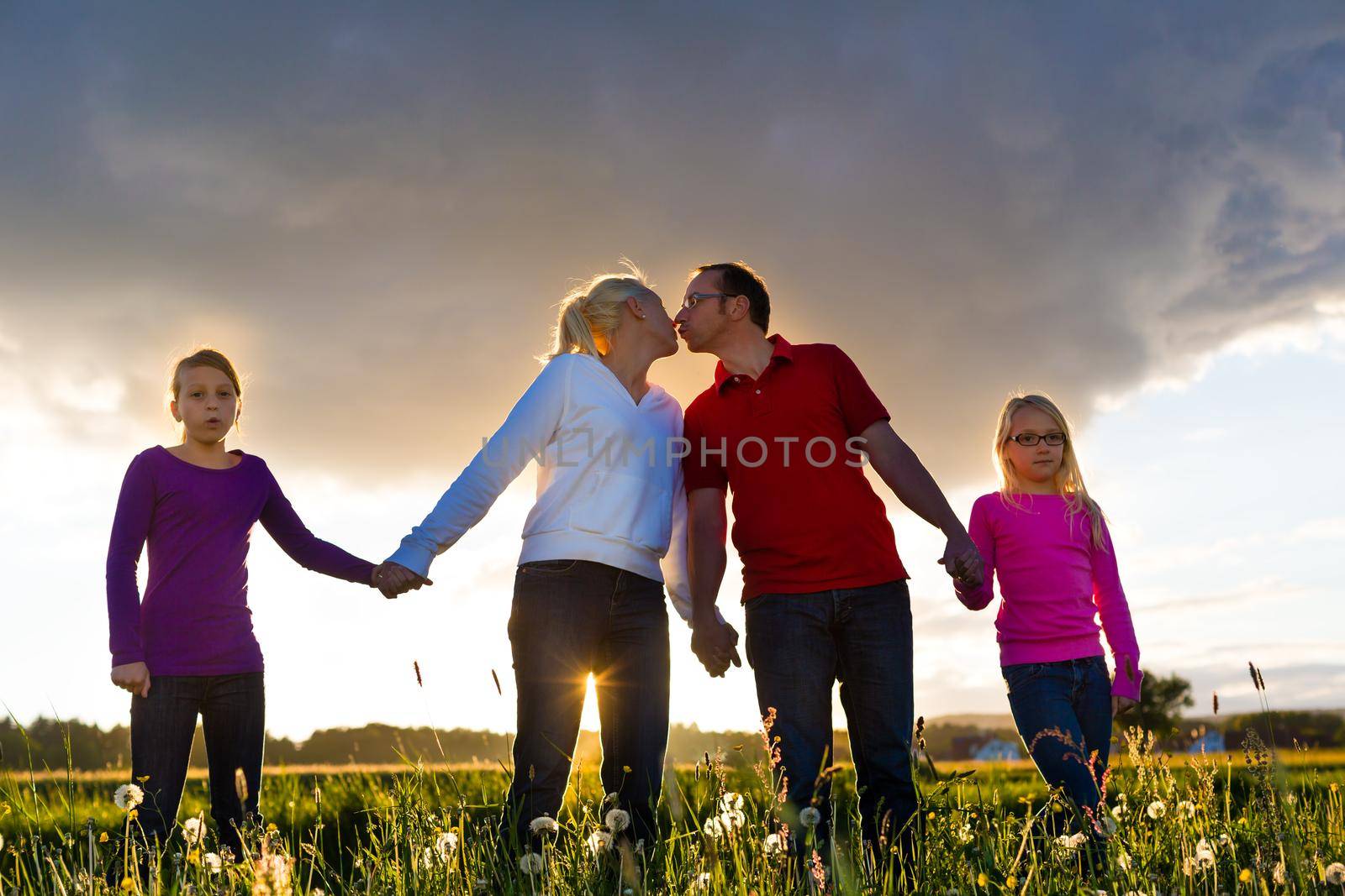 Happy family with daughters standing in the summer meadow at sunset