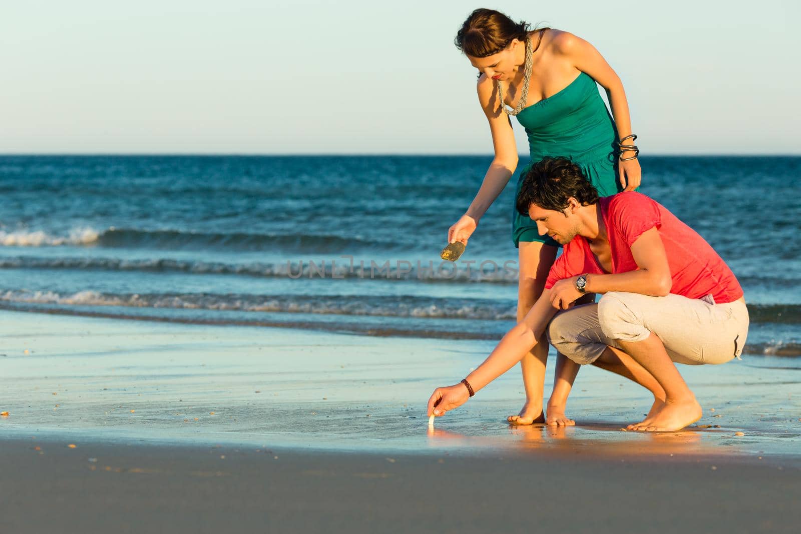 Man and woman, couple, enjoying the romantic sunset on a beach by the ocean in their vacation, they searching shells