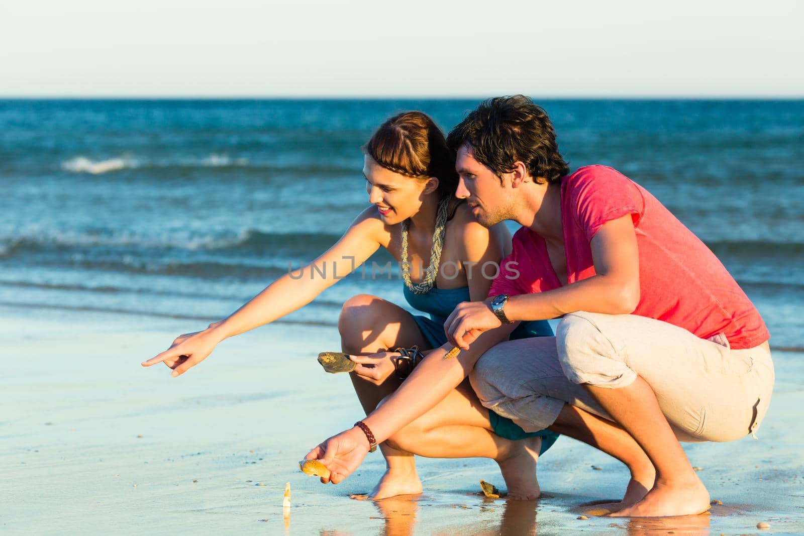 Man and woman, couple, enjoying the romantic sunset on a beach by the ocean in their vacation, they searching shells