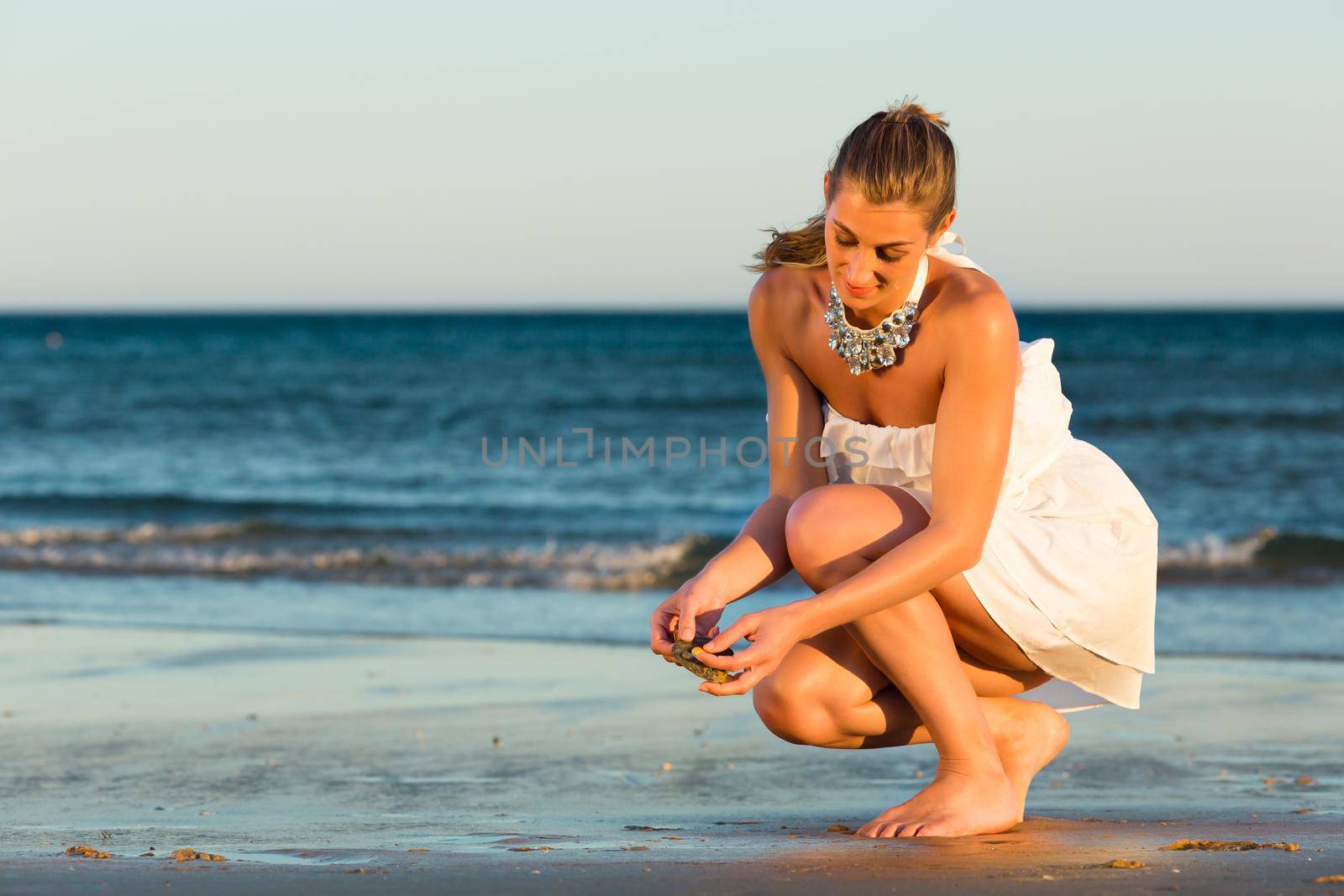 Women looking for sea shells in romantic sunset by Kzenon