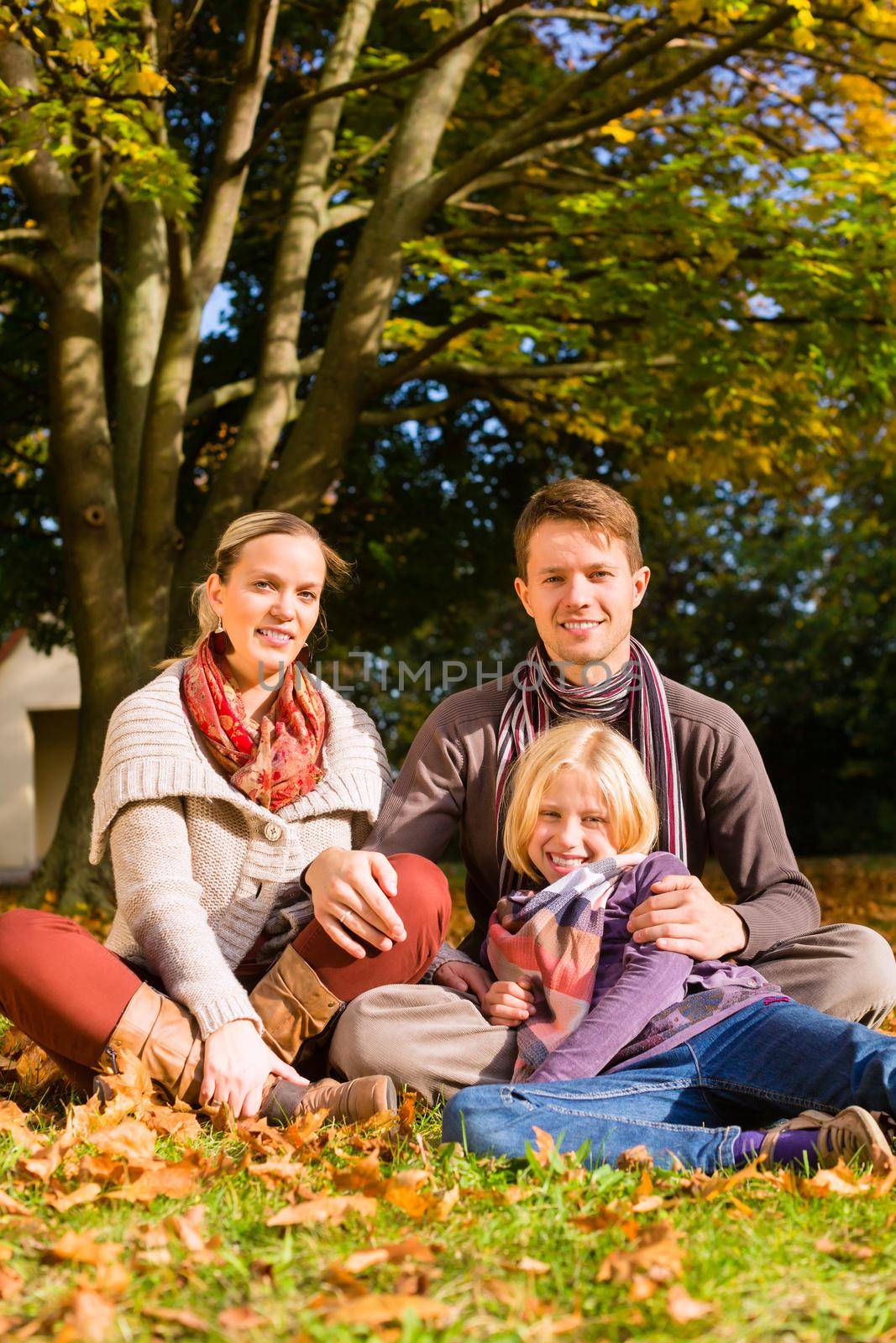 Happy family, Mother, father and daughter or child sitting outdoor on meadow with colorful leaves and under the trees in autumn or fall