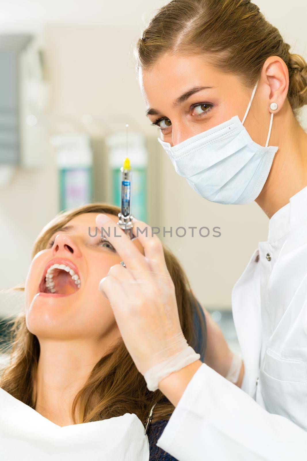 dentist holding a syringe and anesthetizing her patient by Kzenon