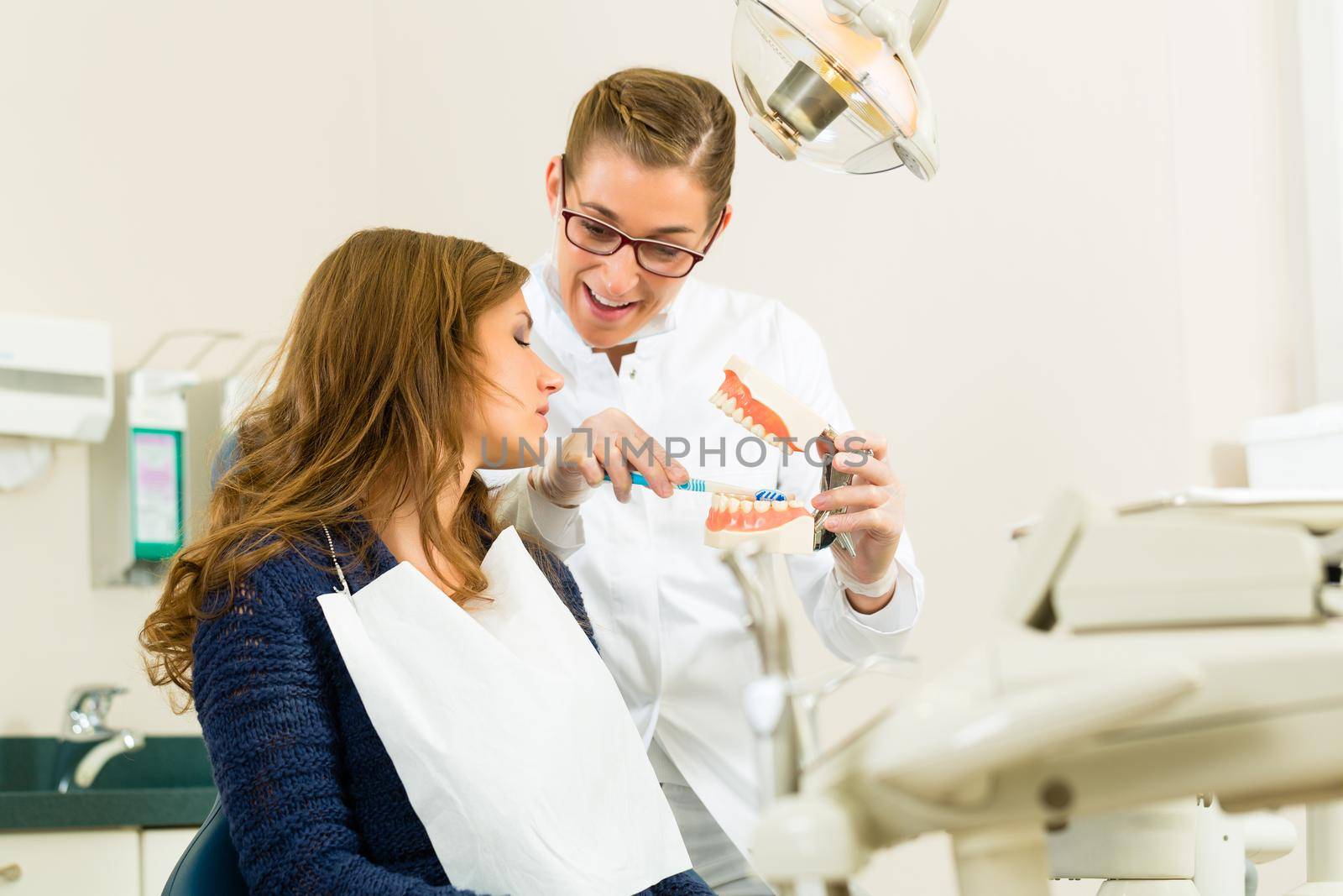 Dentist in his surgery holds a denture and explains a female patient with a toothbrush