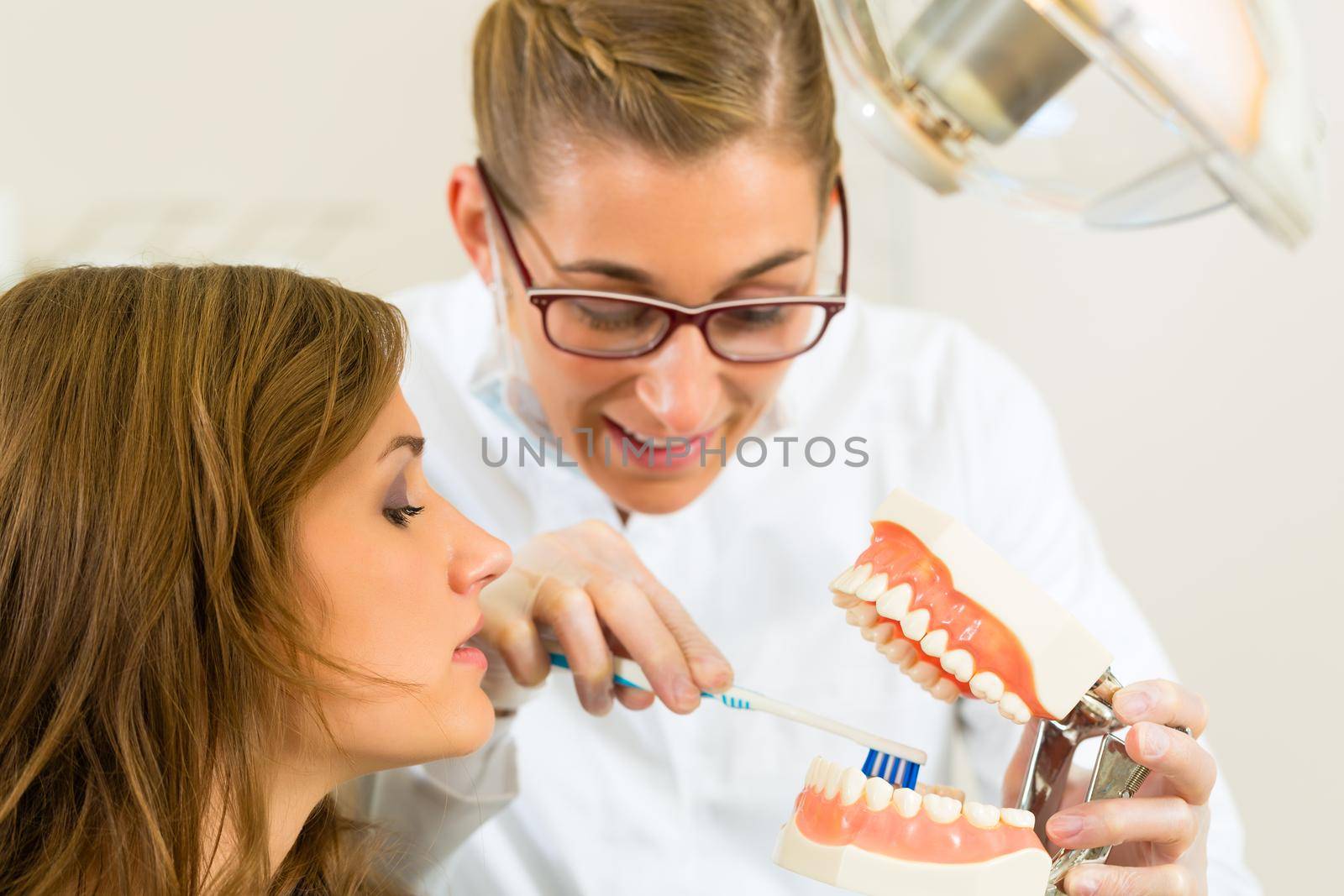 Dentist in his surgery holds a denture and explains a female patient with a toothbrush