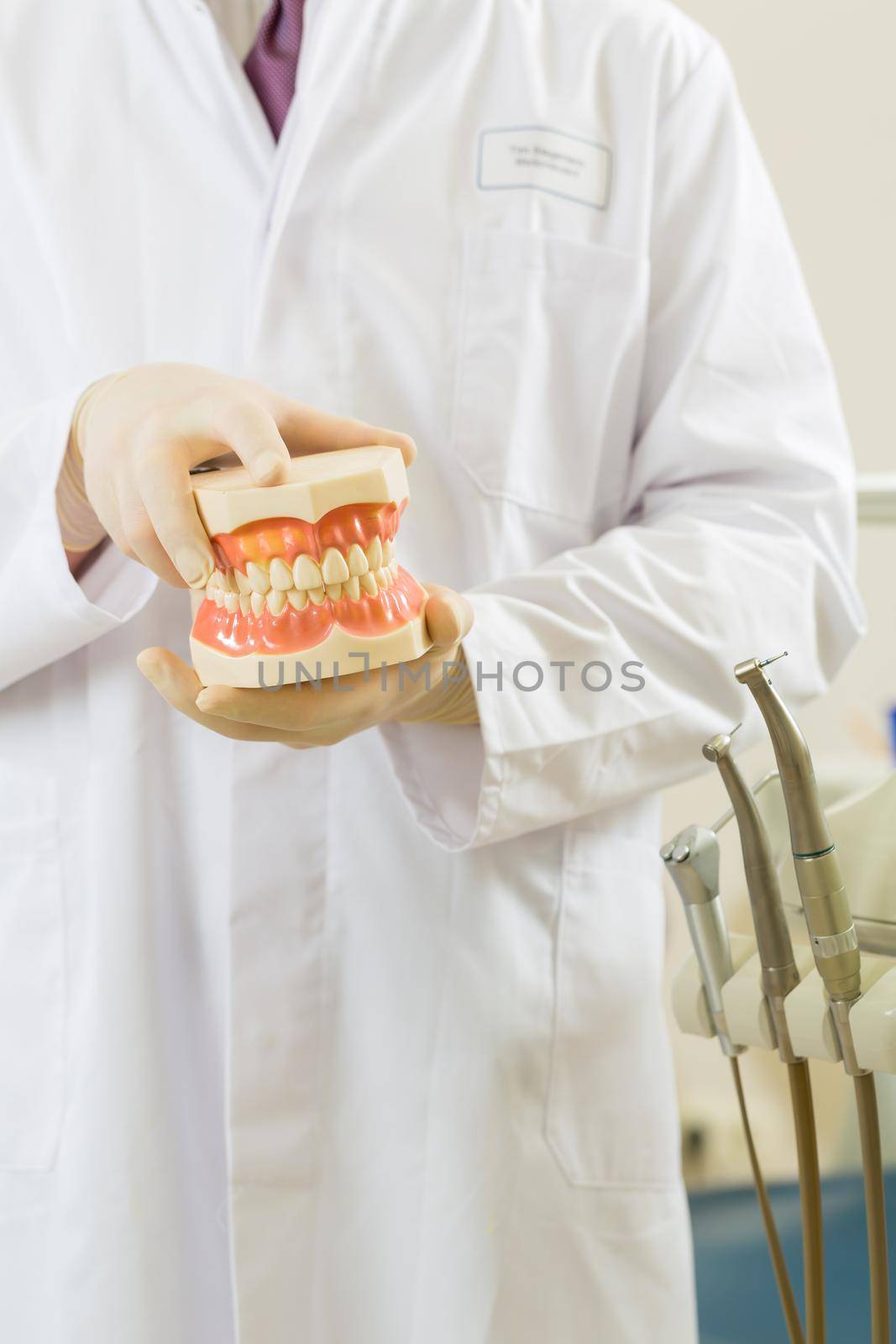 Dentists in his surgery holds a denture, in the background are tools for a dentist