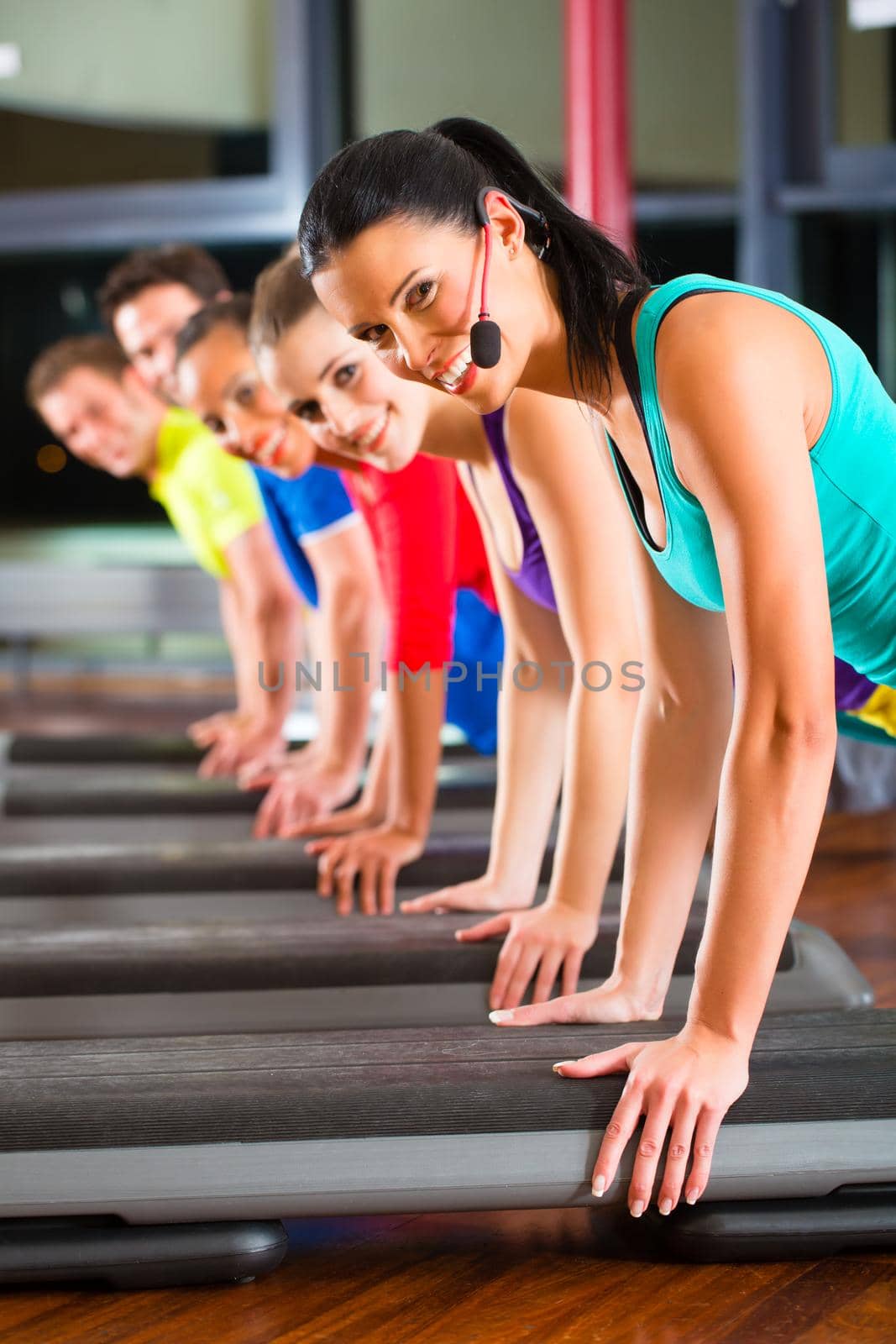 Group of people and instructor in gym stretching by Kzenon