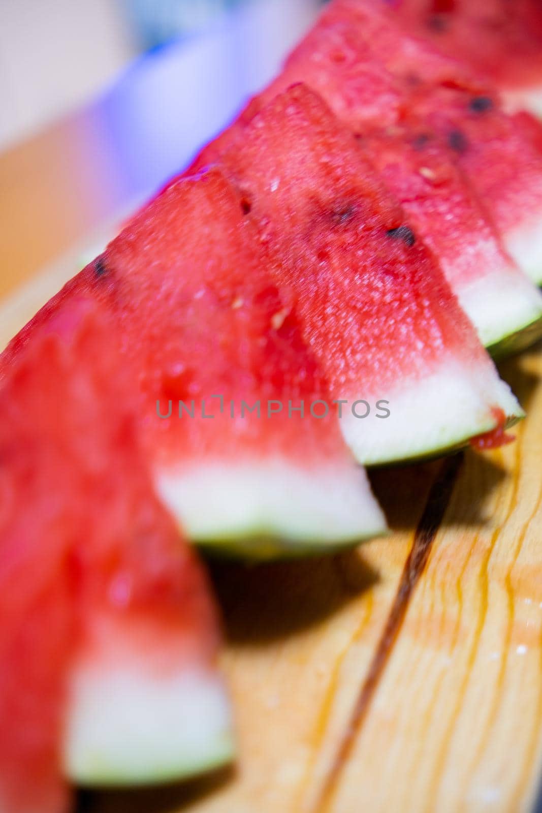 Close-up of fresh and juicy watermelon slices on wooden surface. Row of tasty sliced red tropical fruit on wooden table with blurry background. Healthy food and eating