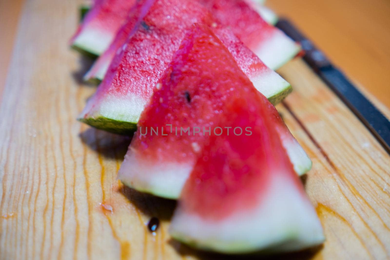 Close-up of fresh and juicy watermelon slices and knife on wooden surface. Row of tasty sliced red tropical fruit on wooden table. Healthy food and eating
