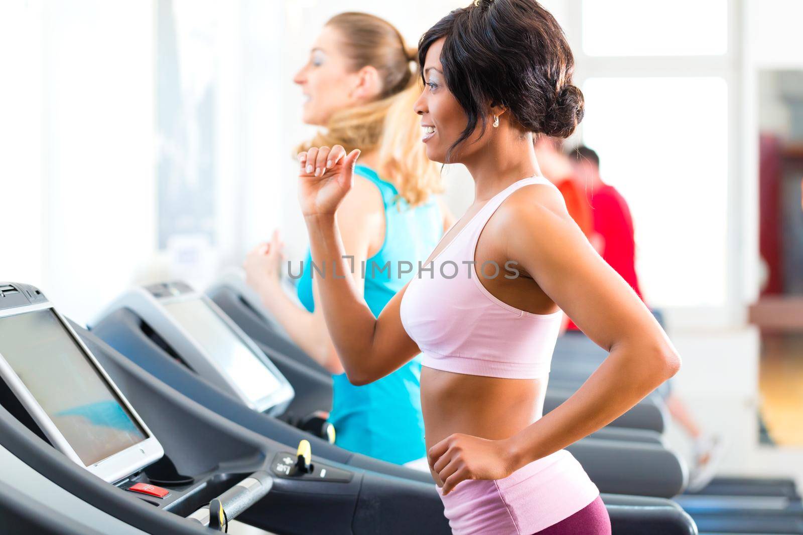 Running on treadmill in gym or fitness club - two women exercising to gain more fitness