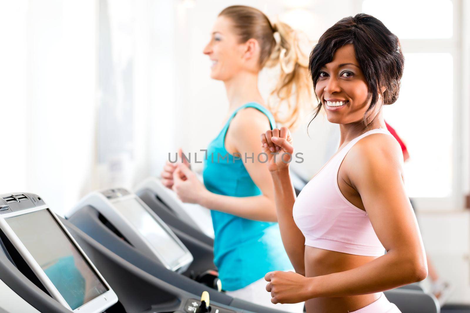 Running on treadmill in gym or fitness club - two women exercising to gain more fitness