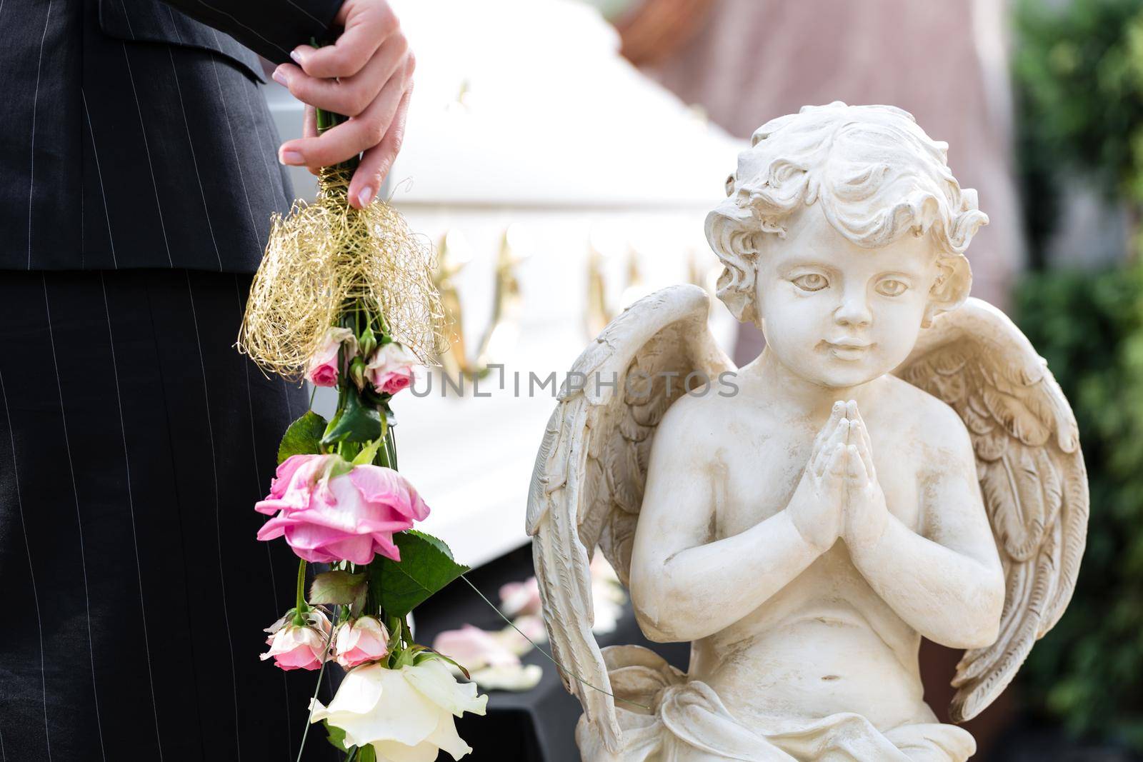 Mourning woman on funeral with pink rose standing at casket or coffin