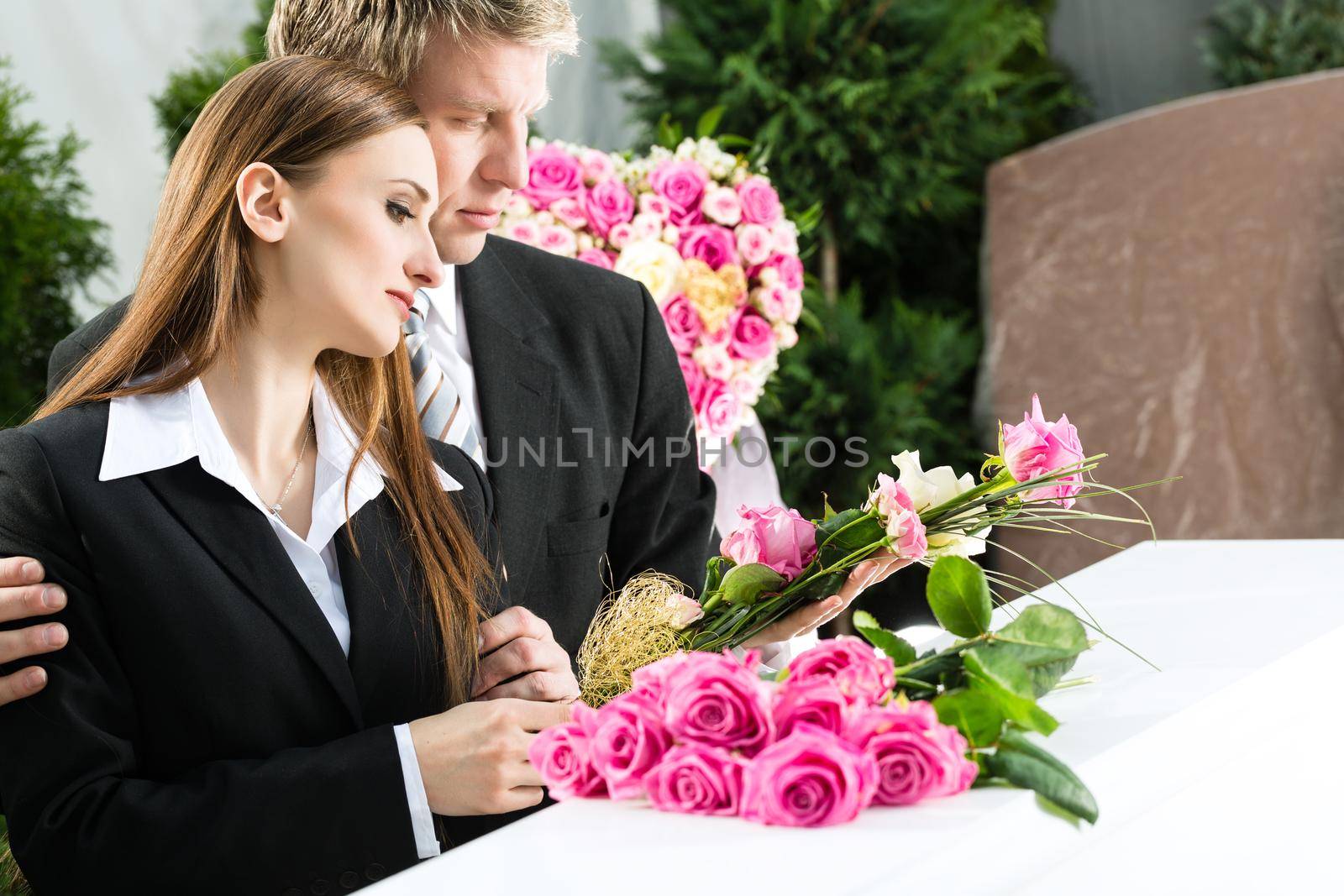 Mourning man and woman on funeral with pink rose standing at casket or coffin