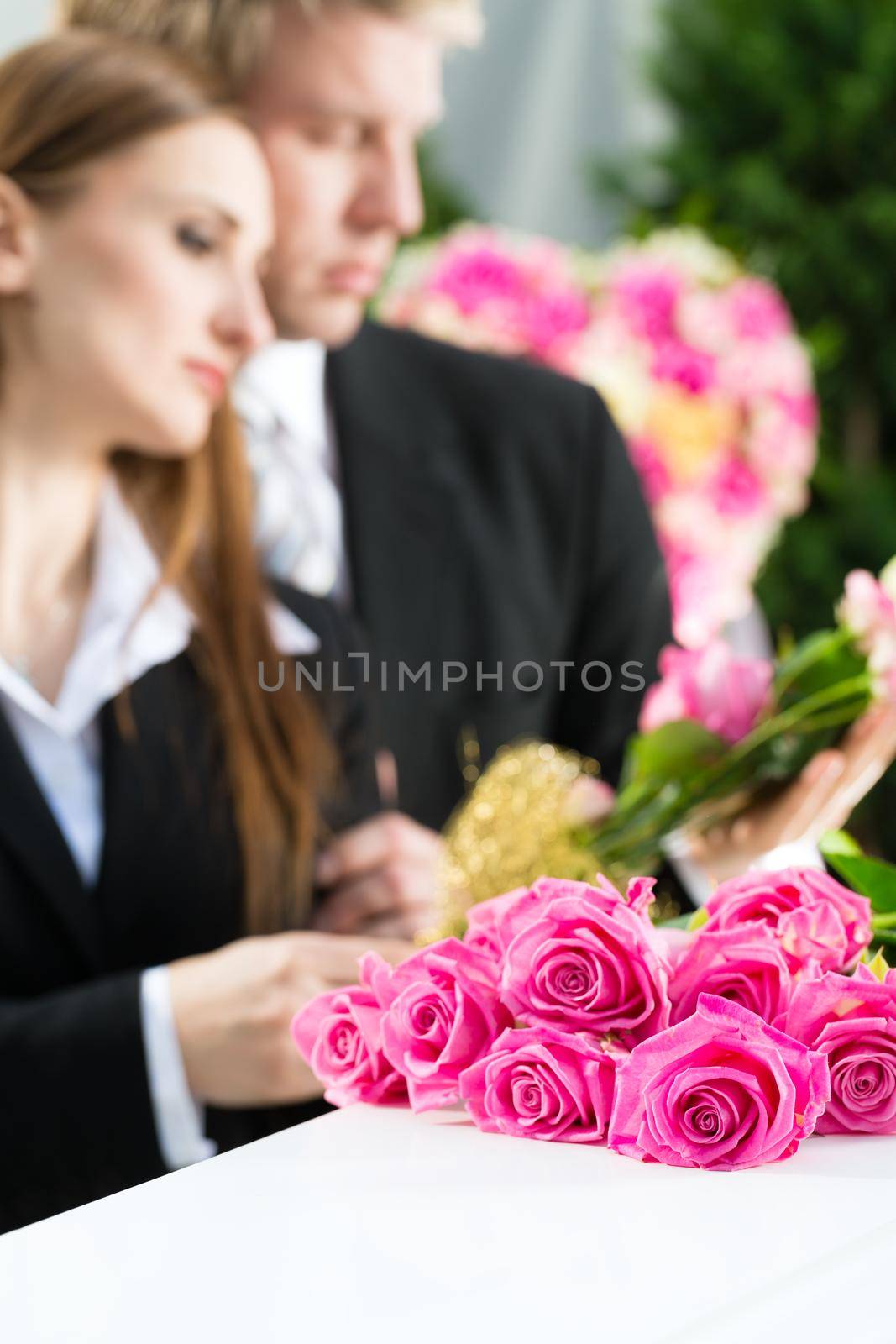 Mourning man and woman on funeral with pink rose standing at casket or coffin