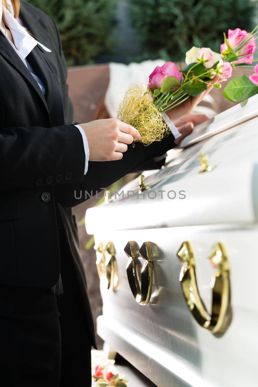 Mourning man and woman on funeral with pink rose standing at casket or coffin