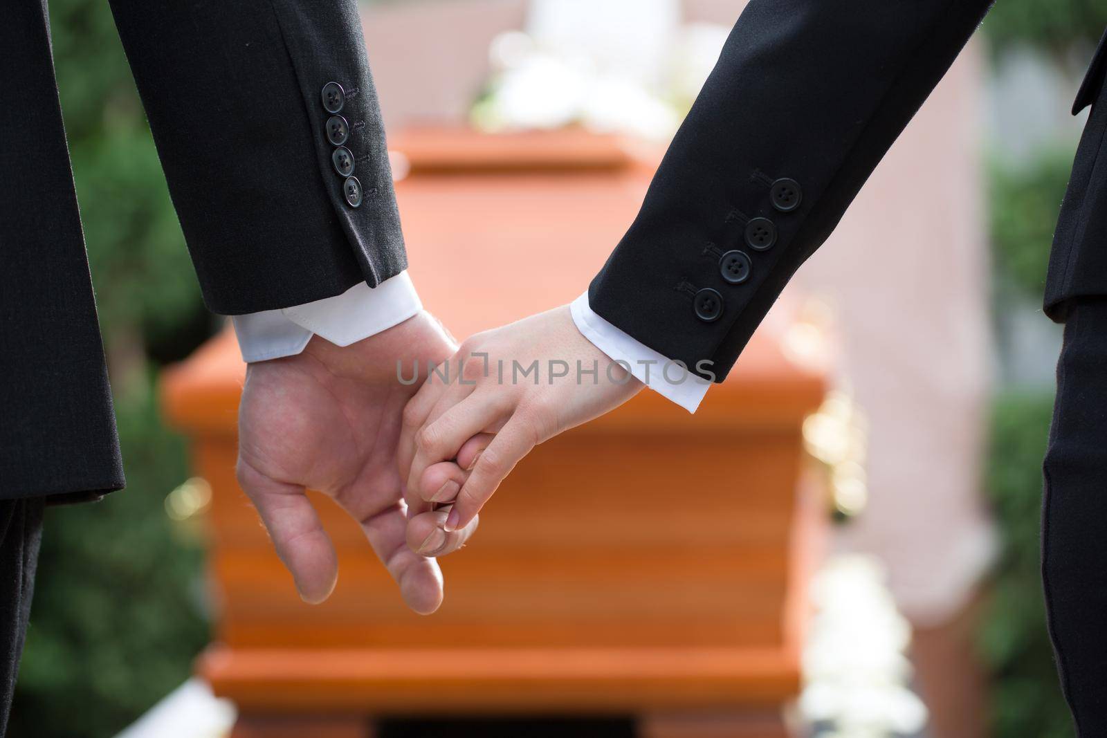 Religion, death and dolor - couple at funeral holding hands consoling each other in view of the loss