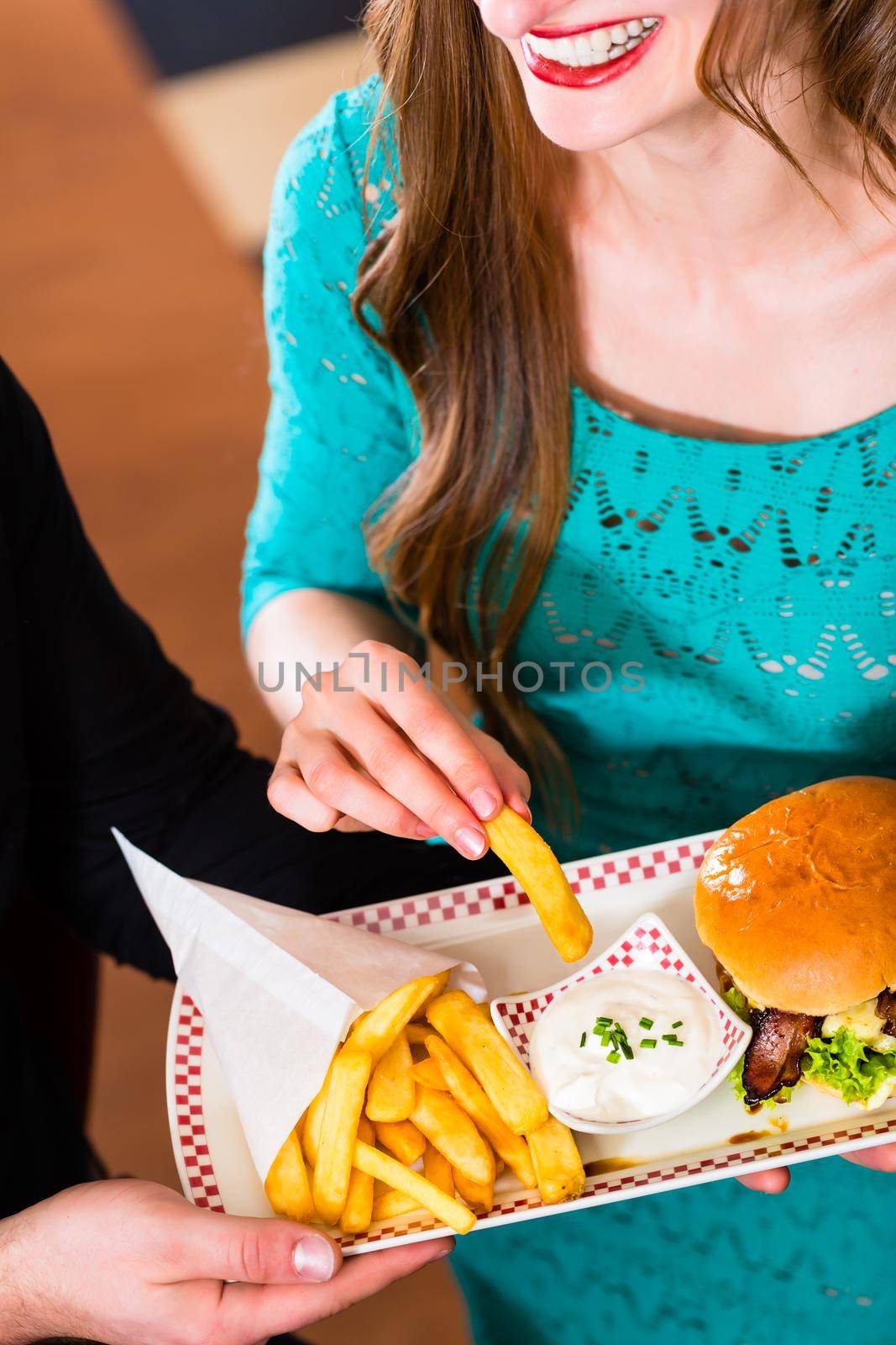 Friends or couple eating fast food with burger and fries by Kzenon