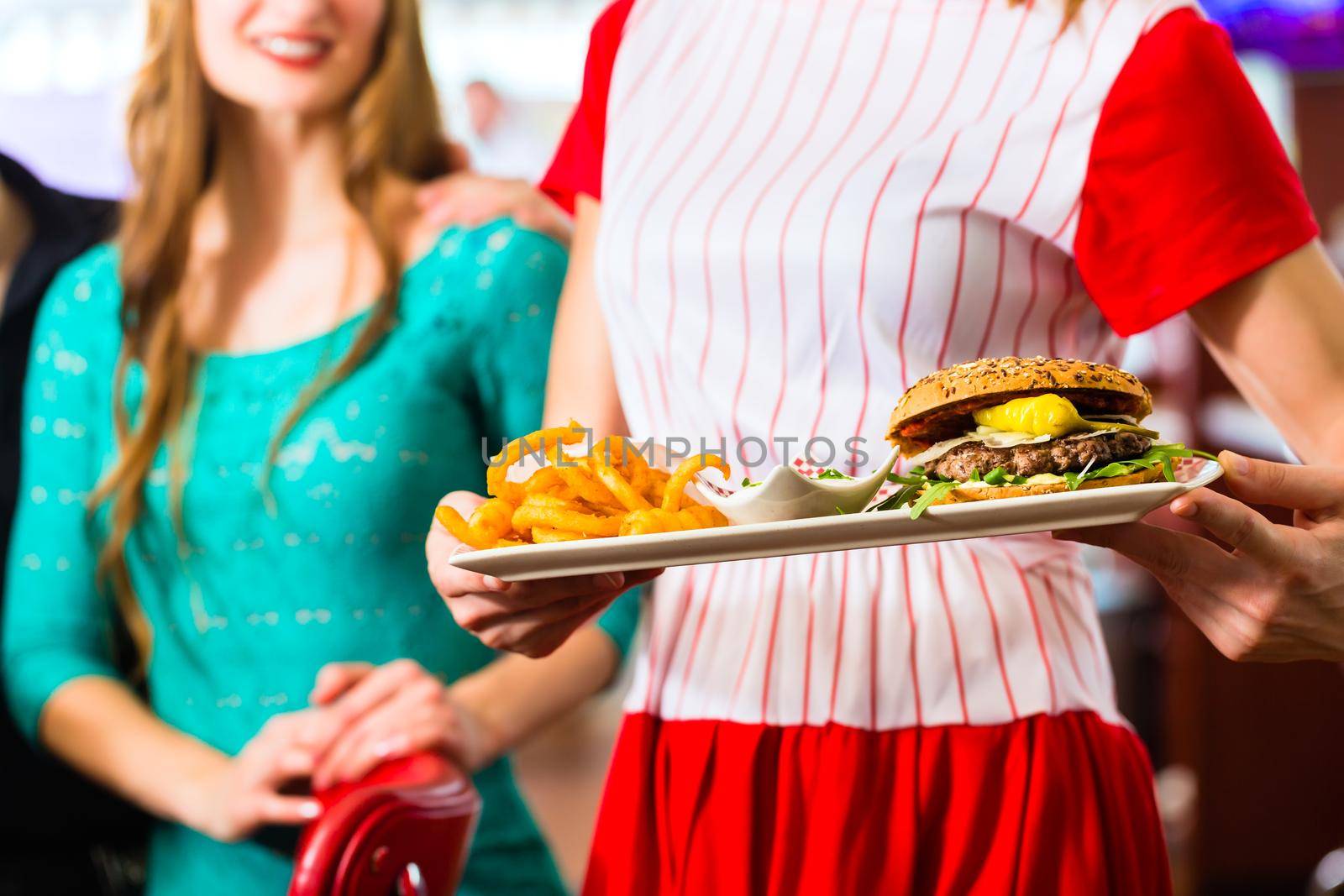 Friends or couple eating fast food in American fast food diner, the waitress wearing a short costume serving a meal