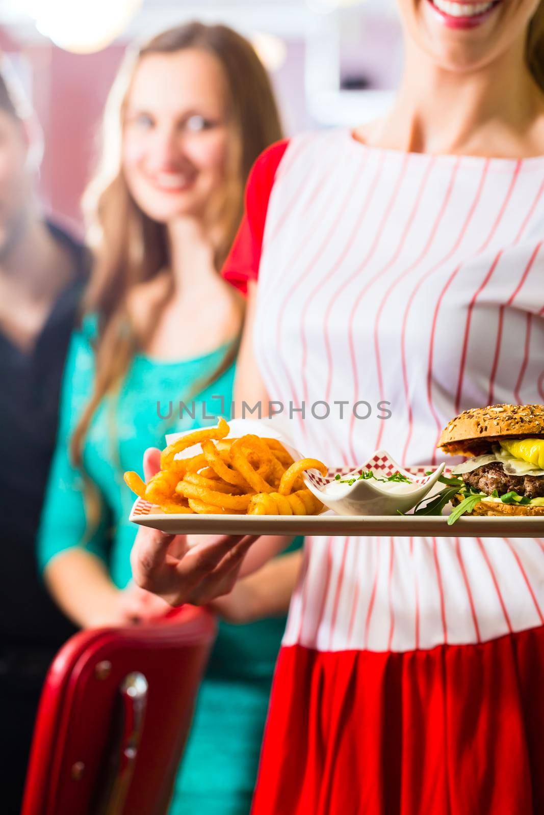 Friends or couple eating fast food in American fast food diner, the waitress wearing a short costume serving a meal