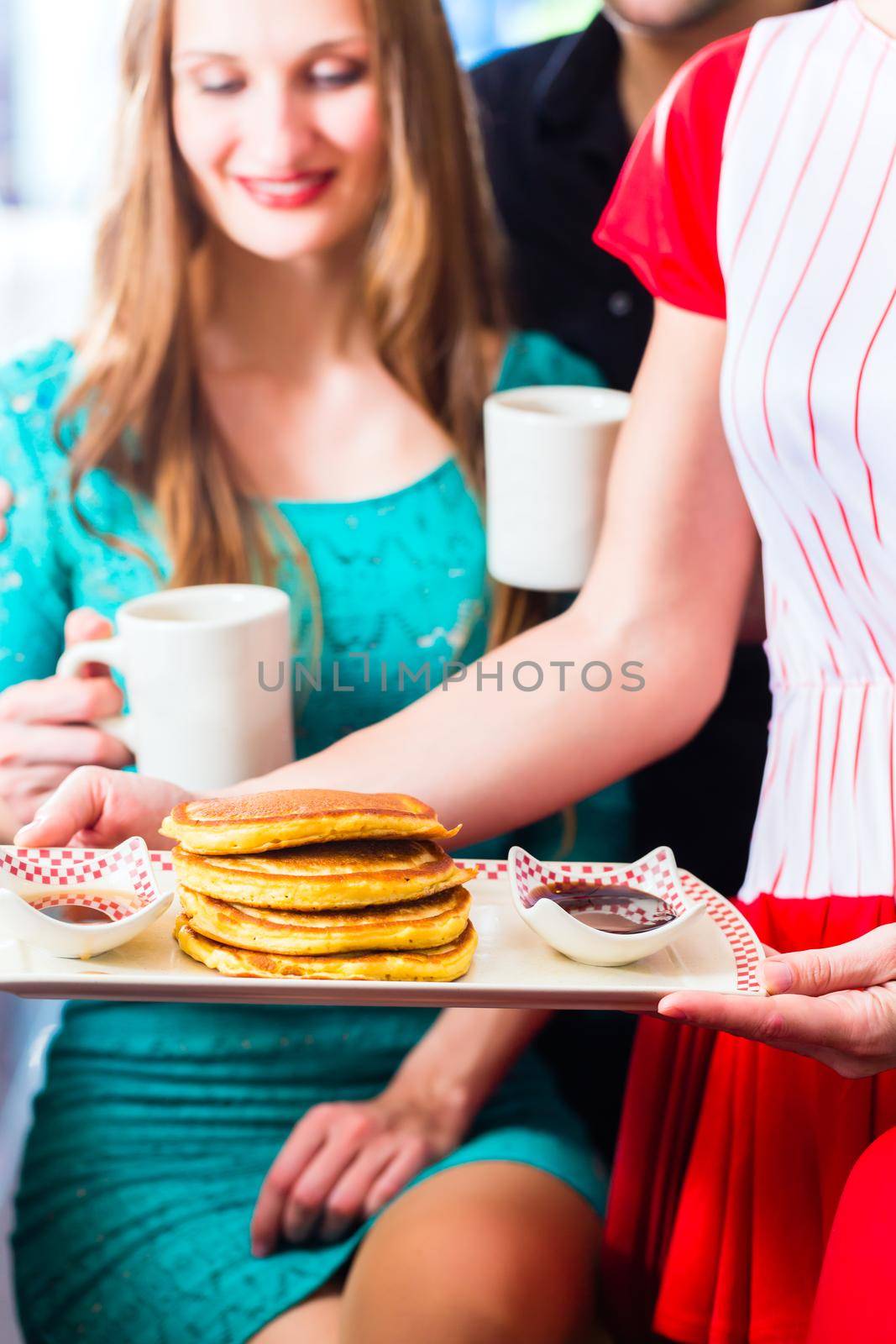 Friends or couple eating fast food for breakfast with pancakes and coffee in American fast food diner, the waitress serving the food