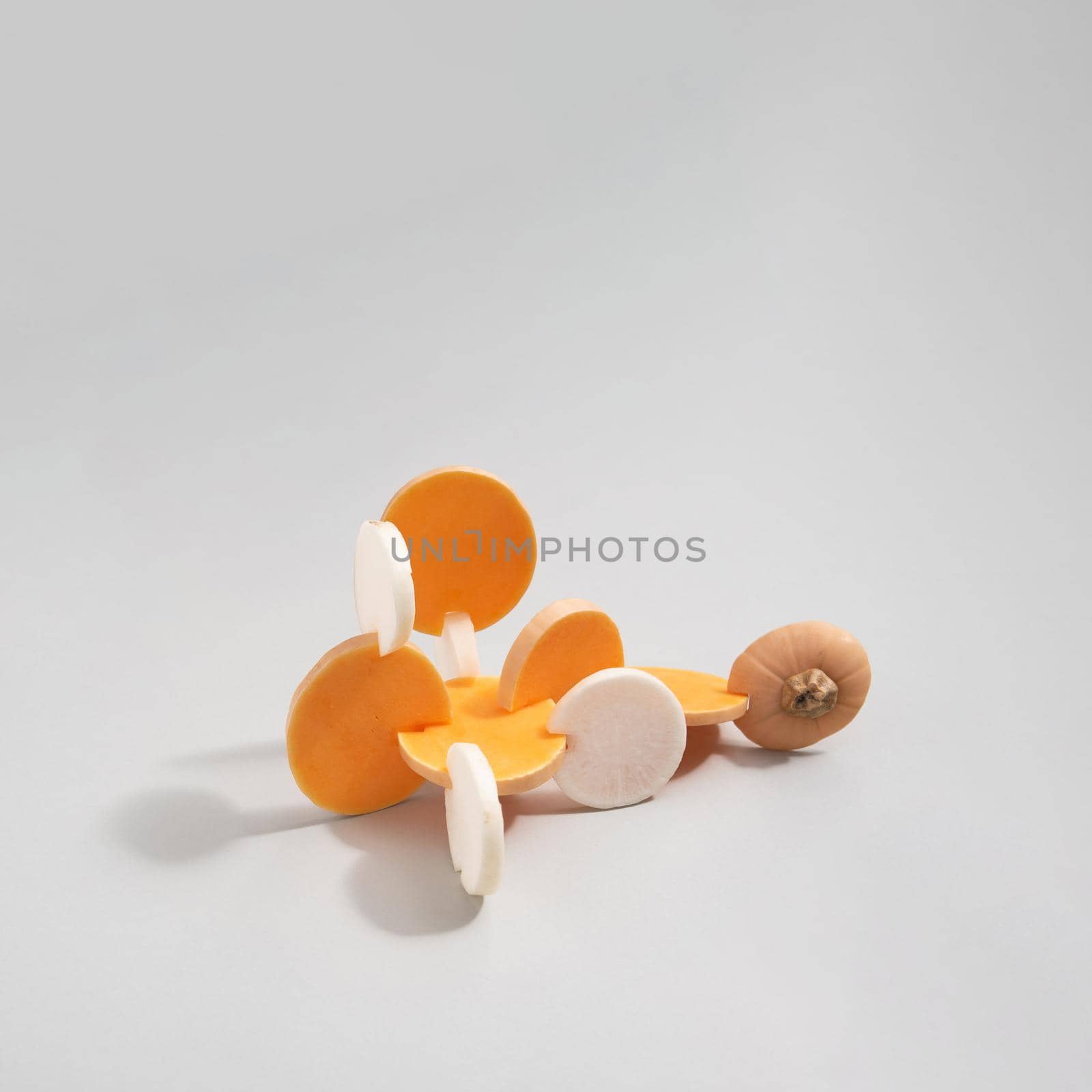 Abstract composition made of sliced butternut squash and white radish isolated on grey background. Square layout with copy space