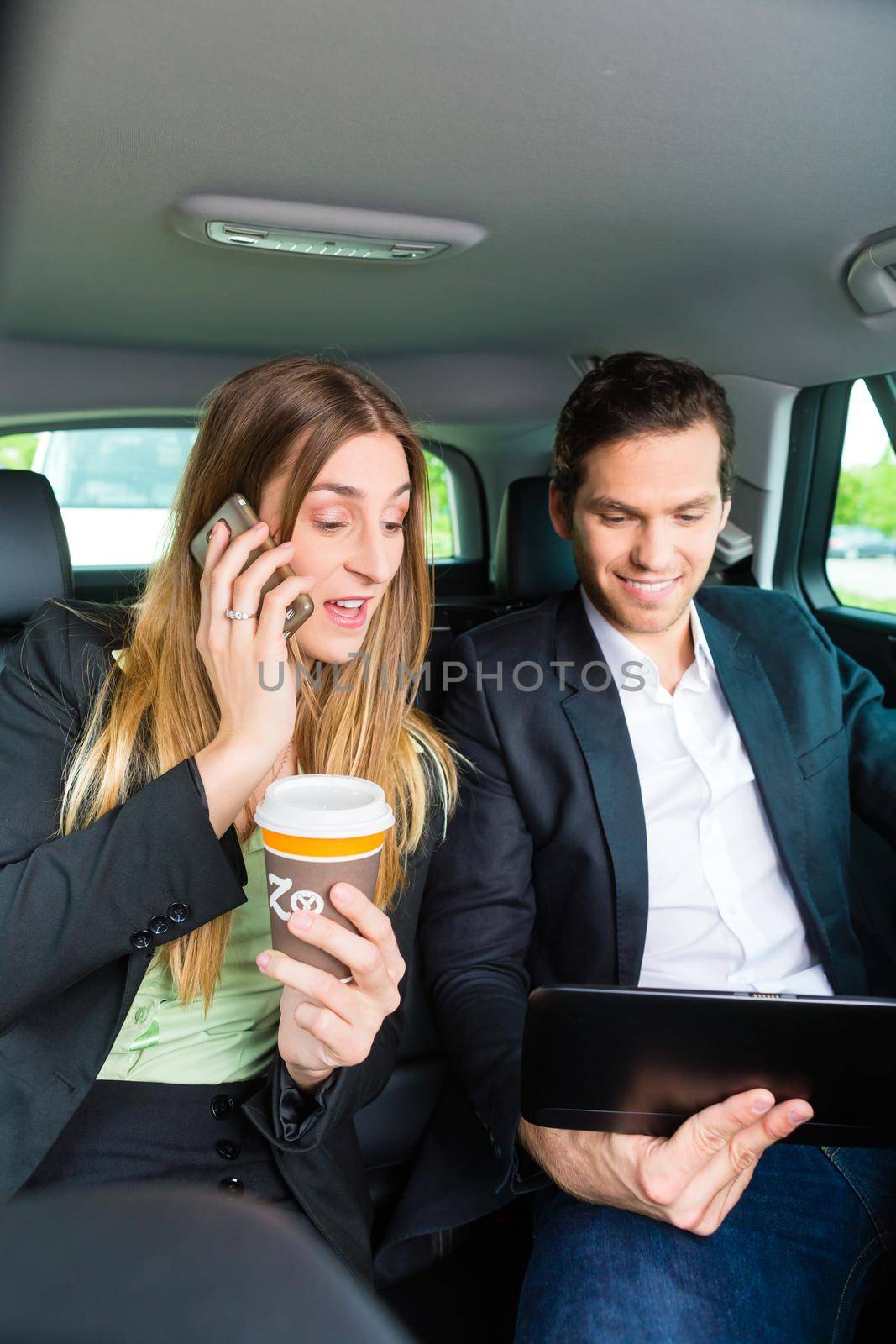 Young businesspeople with mobile phone and tablet computer traveling in taxi, they are colleagues