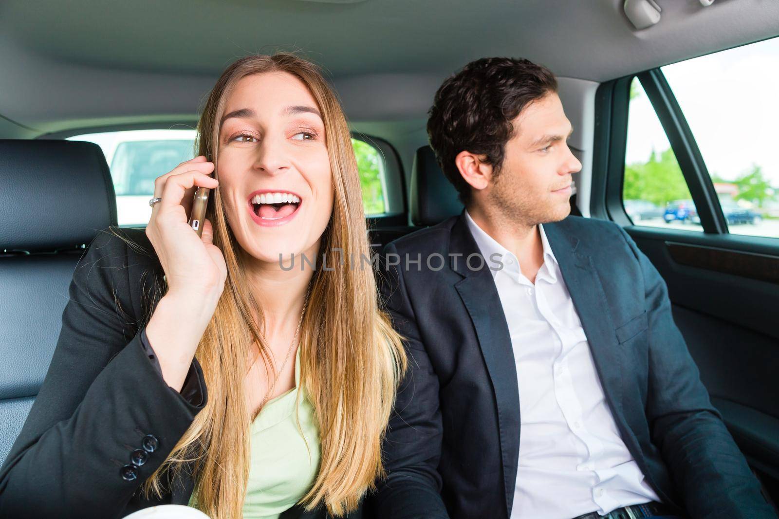 Young businesspeople traveling in taxi, she is busy on the phone, they are colleagues