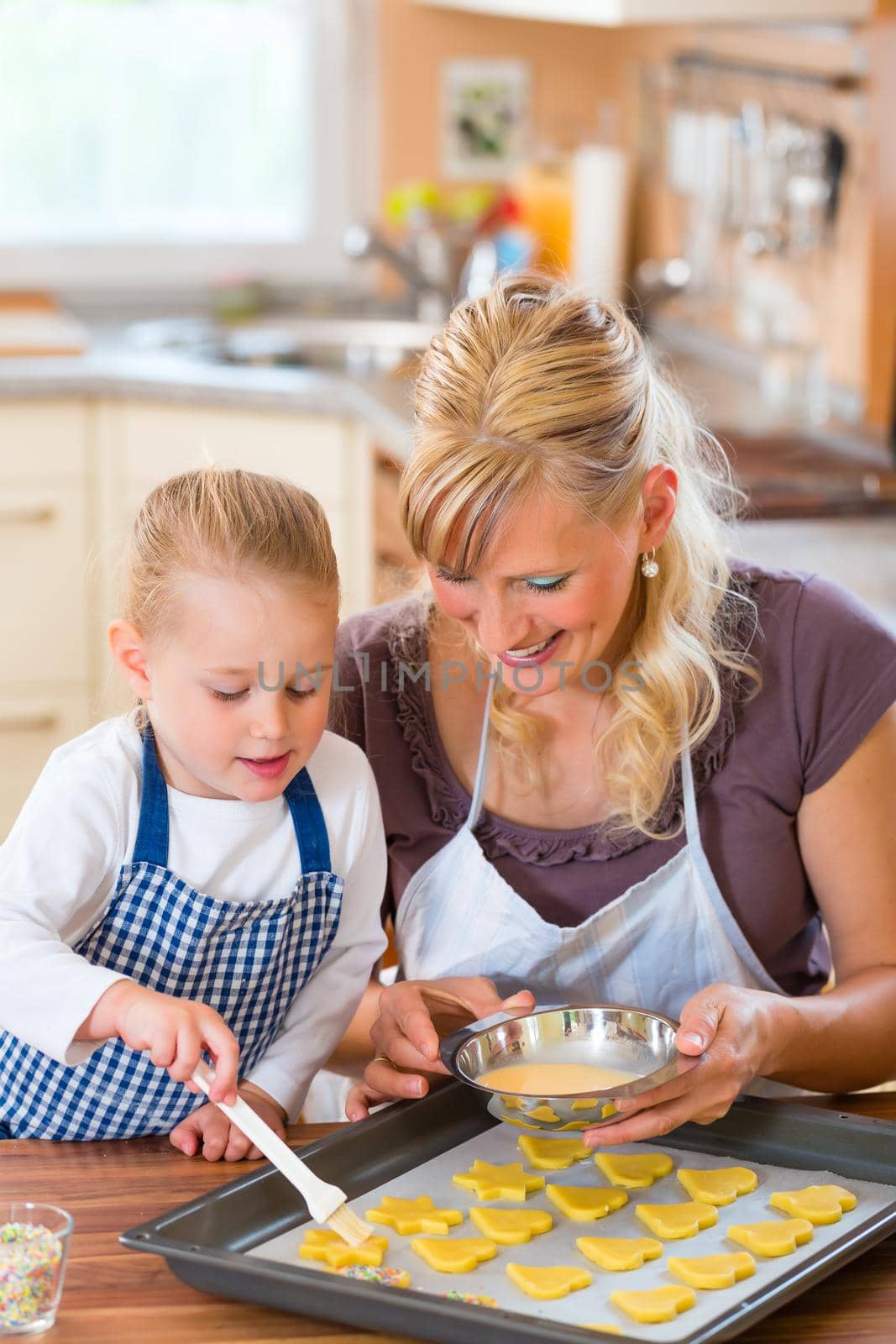 Baking with the family - Mother and daughter coat self made cookies with a brush