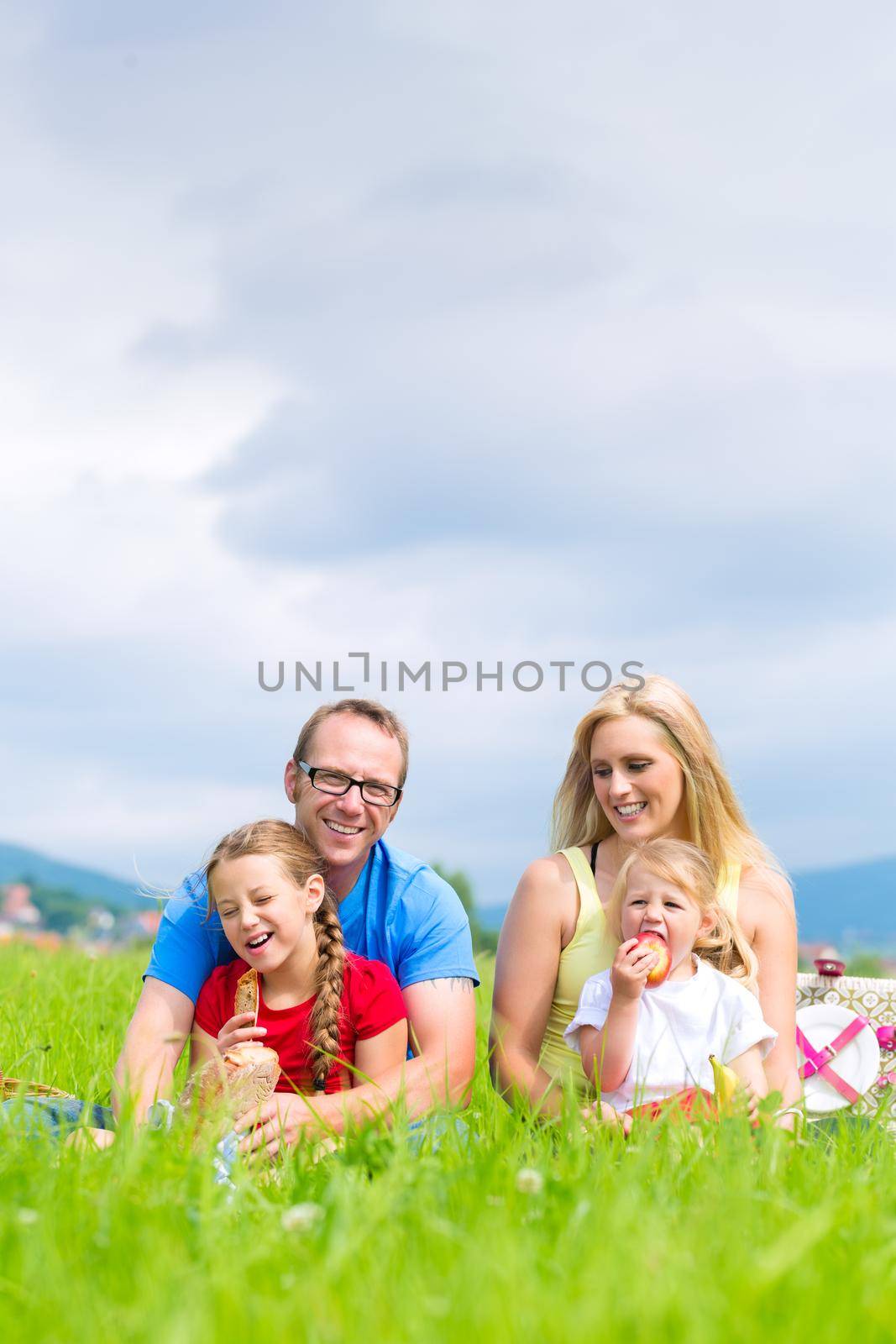 Happy family with daughter or kids sitting in a meadow in summer eating food on picnic