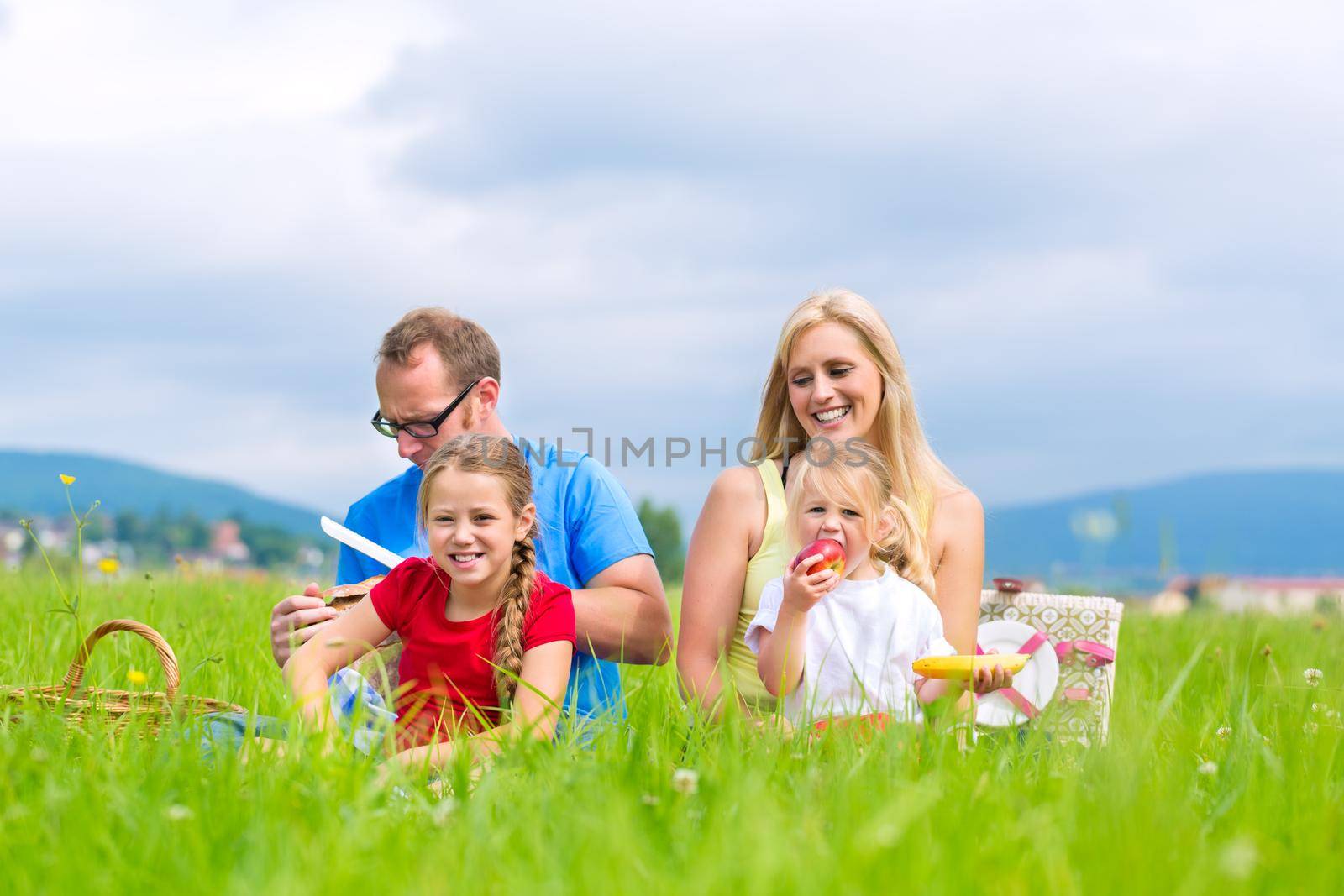 Happy family having picnic in meadow by Kzenon