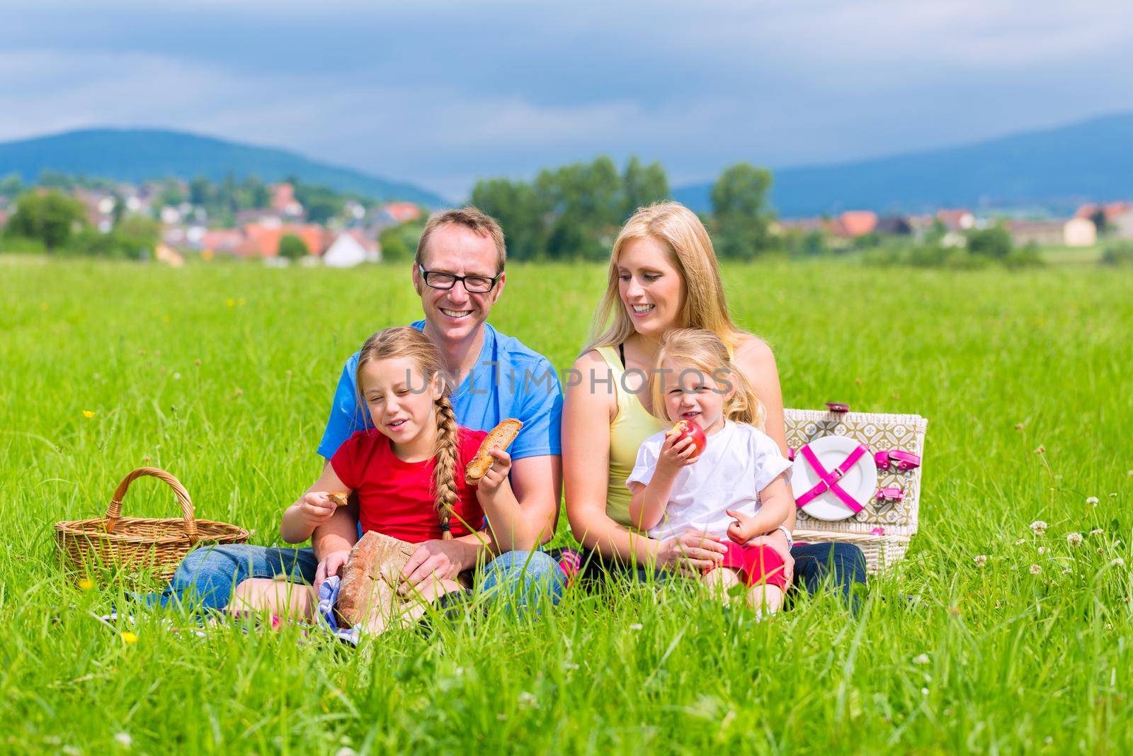 Happy family with daughter or kids sitting in a meadow in summer eating food on picnic