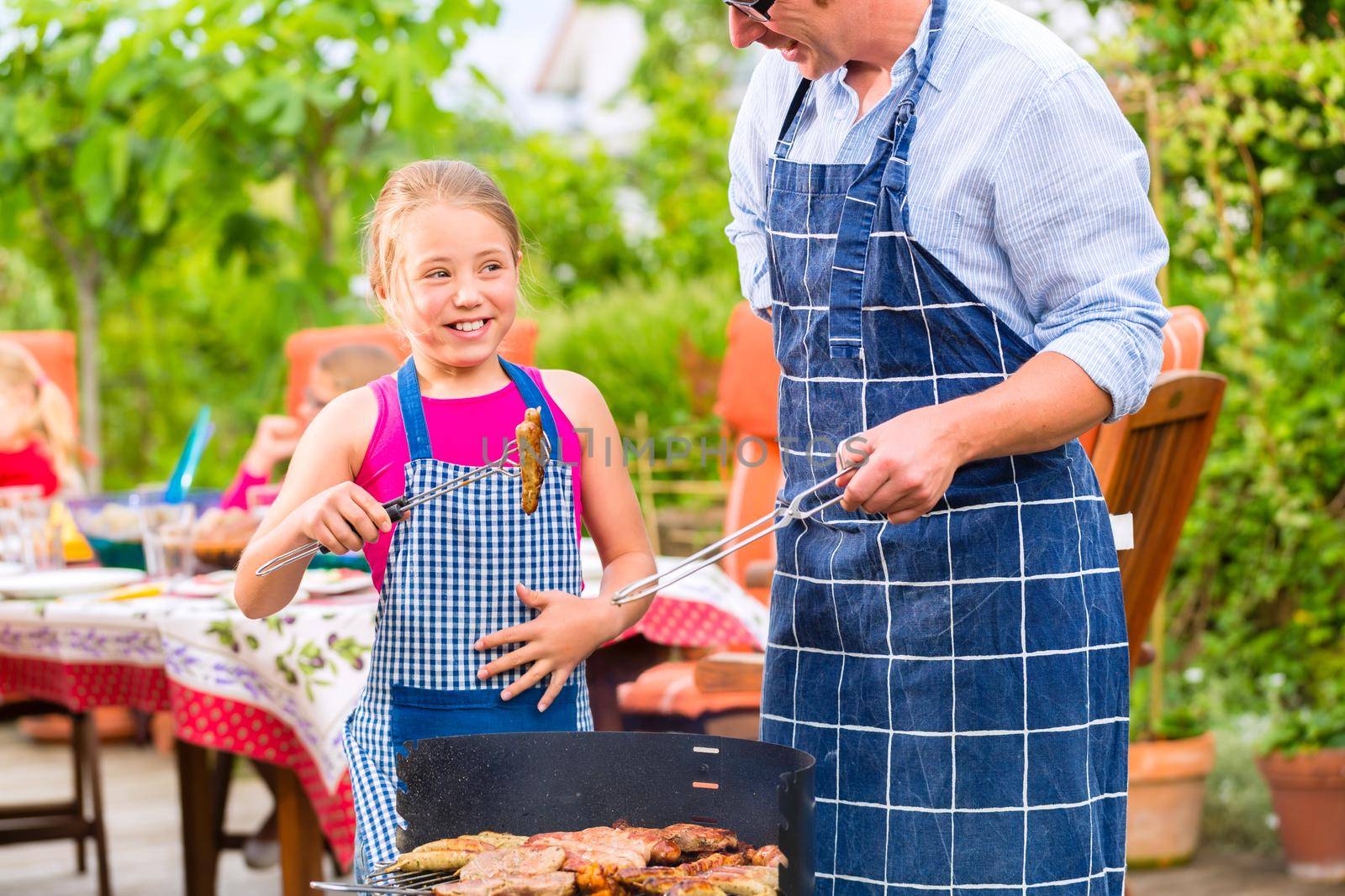 Father and daughter making barbecue in the garden in summer with sausages and meat