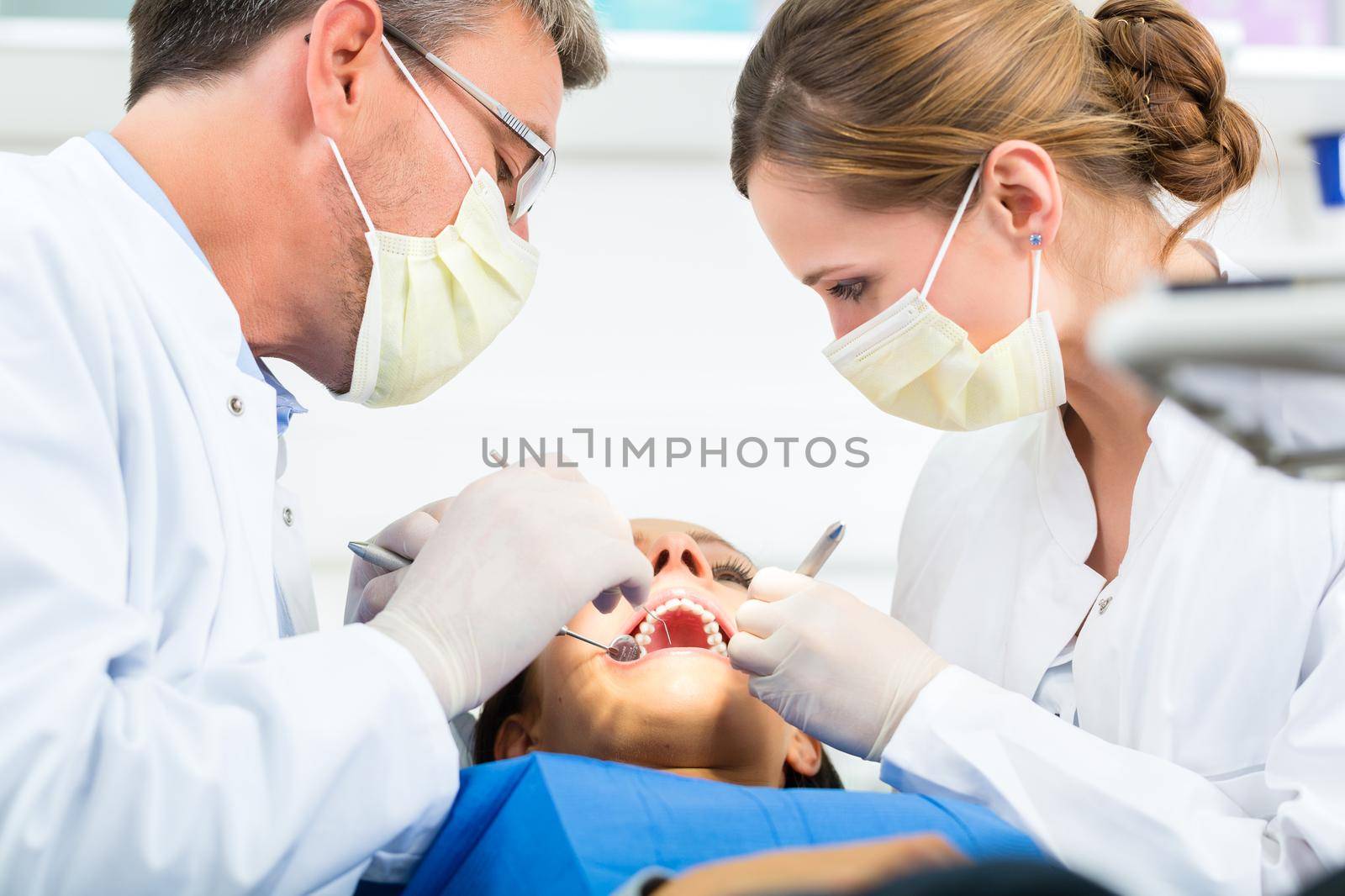 Female patient with dentist and assistant in a dental treatment, wearing masks and gloves