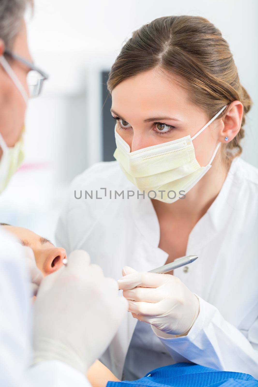 Female patient with dentist and assistant in a dental treatment, wearing masks and gloves