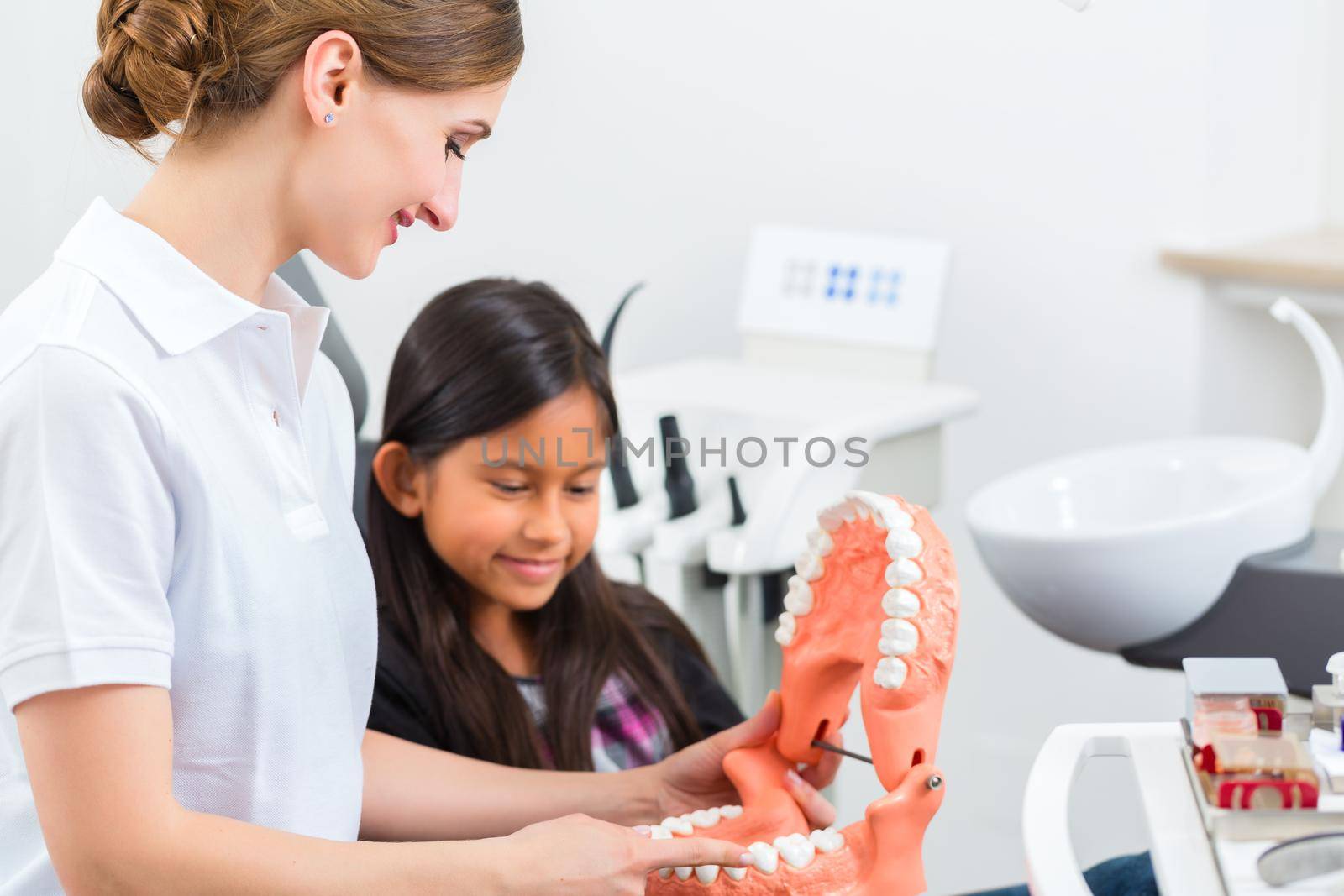 Dentist in surgery holds denture and explains a child patient with a toothbrush