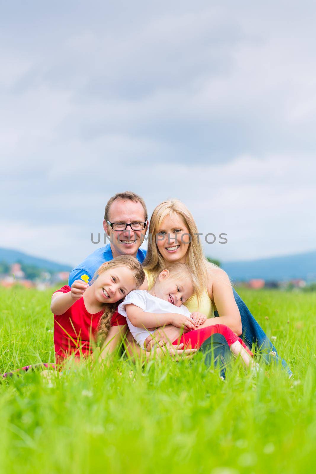 Happy family of Mother, father and kids or daughter and sisters or siblings sitting outdoor on meadow