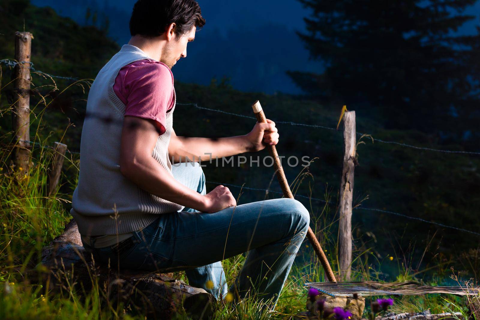 Tyrol - Young man sitting on alpine meadow of a mountain on Campfire in the Bavarian Alps and enjoys the romantic evening sunset of the panorama in leisure time or vacation