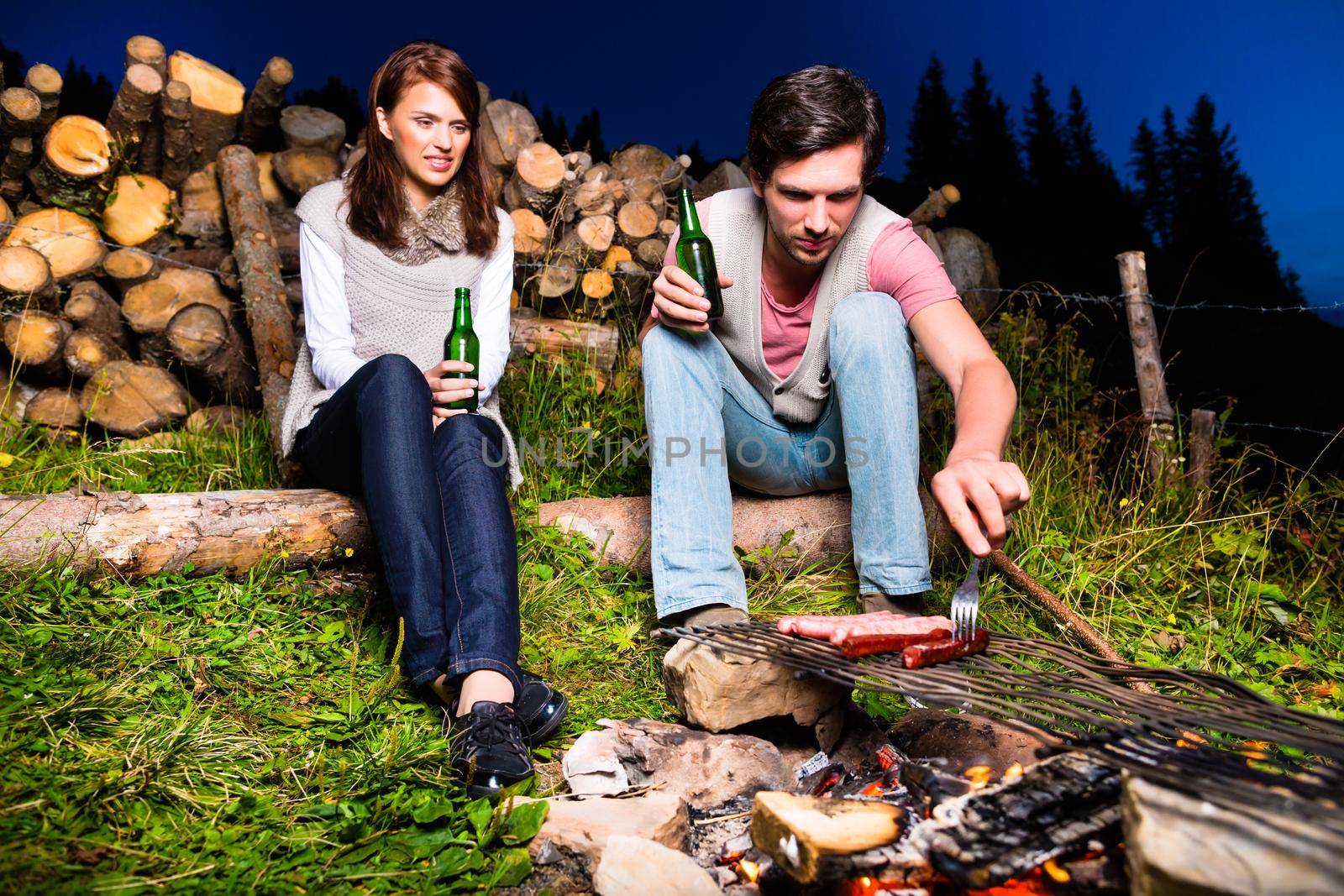 Tyrol - Young couple sitting on alpine meadow of a mountain on Campfire in the Bavarian Alps enjoying the romantic evening sunset of the panorama in leisure time or vacation