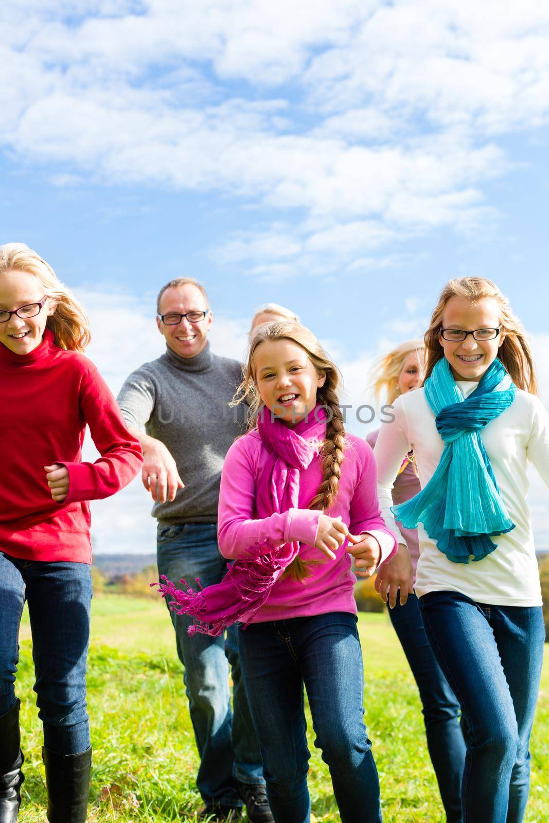 Family running through park in fall or autumn by Kzenon