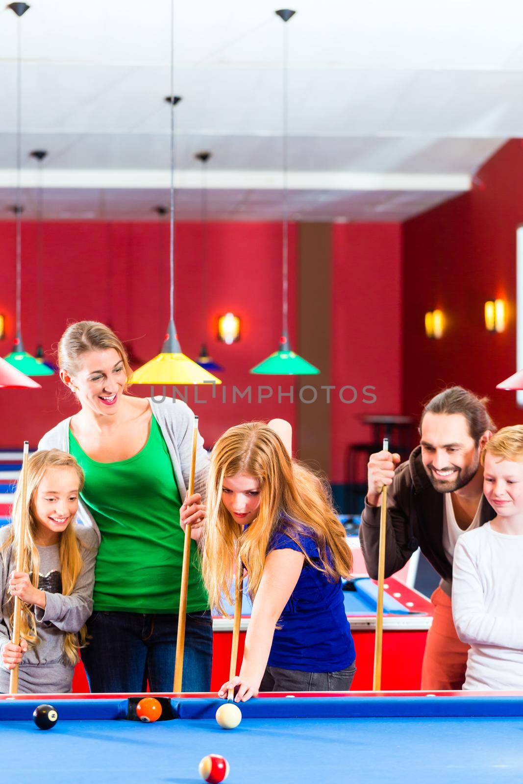 Family playing together billiard with queue and balls on pool table