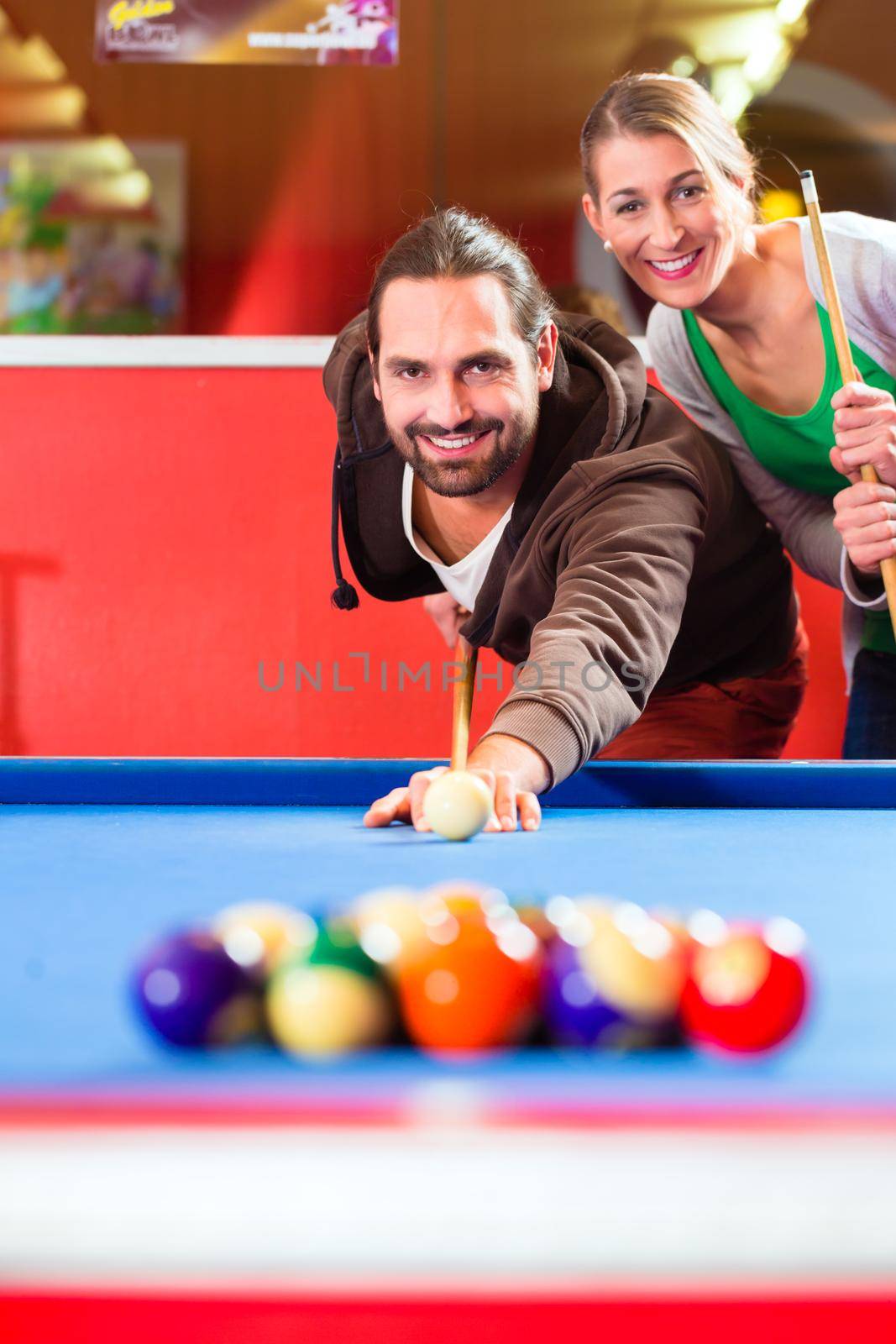 Couple or friends playing billiard with queue and balls on pool table