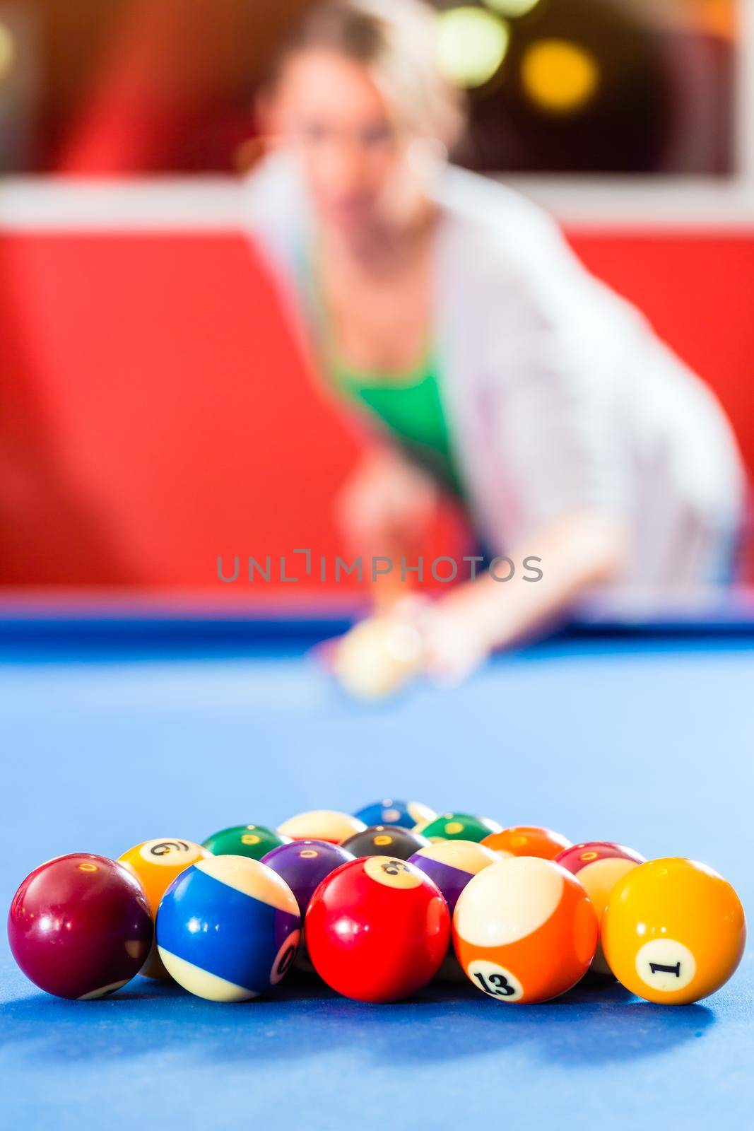 Couple or friends playing billiard with queue and balls on pool table