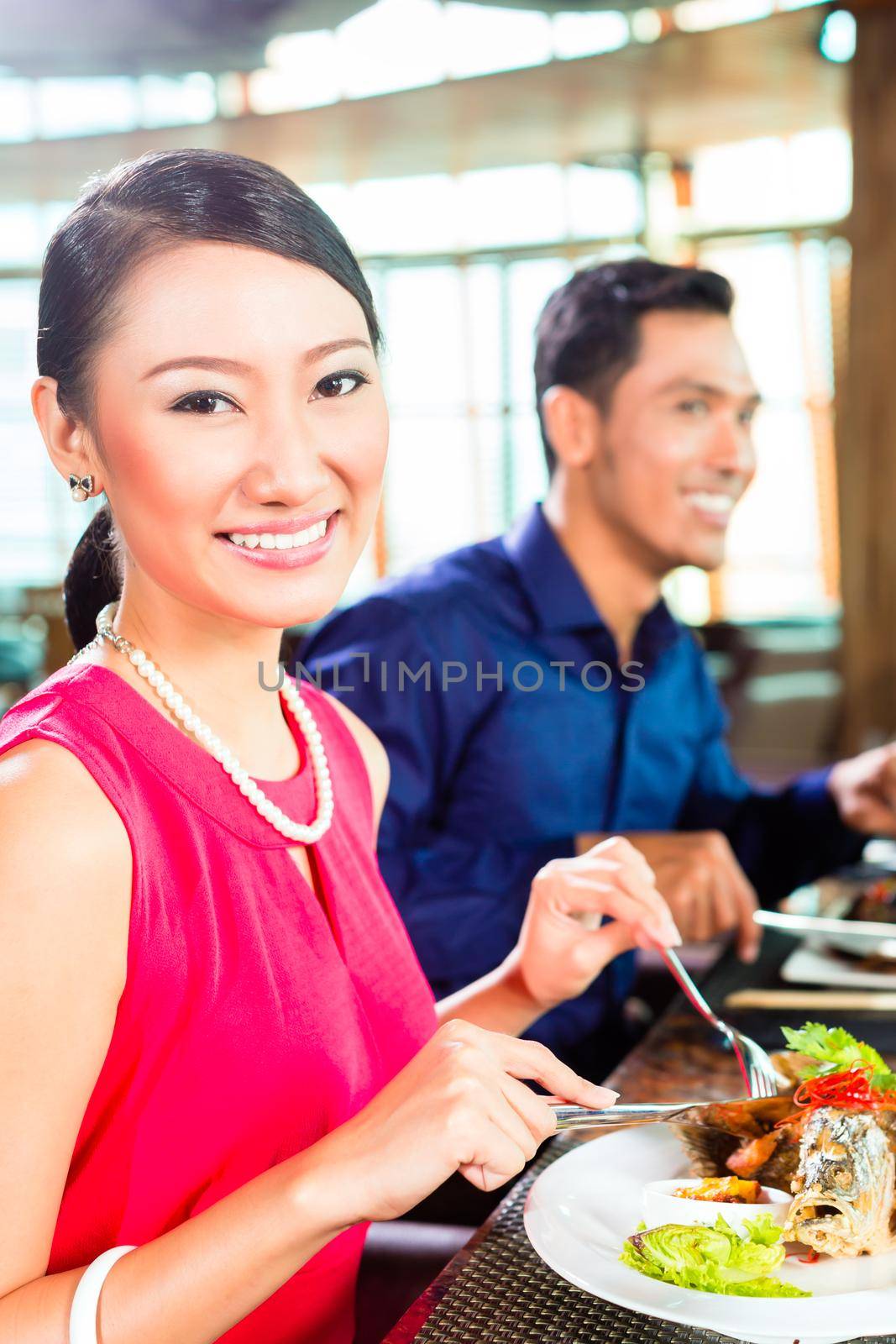 Asian people having dinner and drinking red wine in very fancy restaurant with open kitchen in background