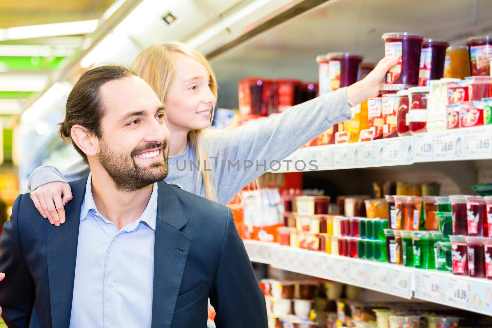 Father carrying daughter on his back while she is selecting dessert at grocery shopping in supermarket