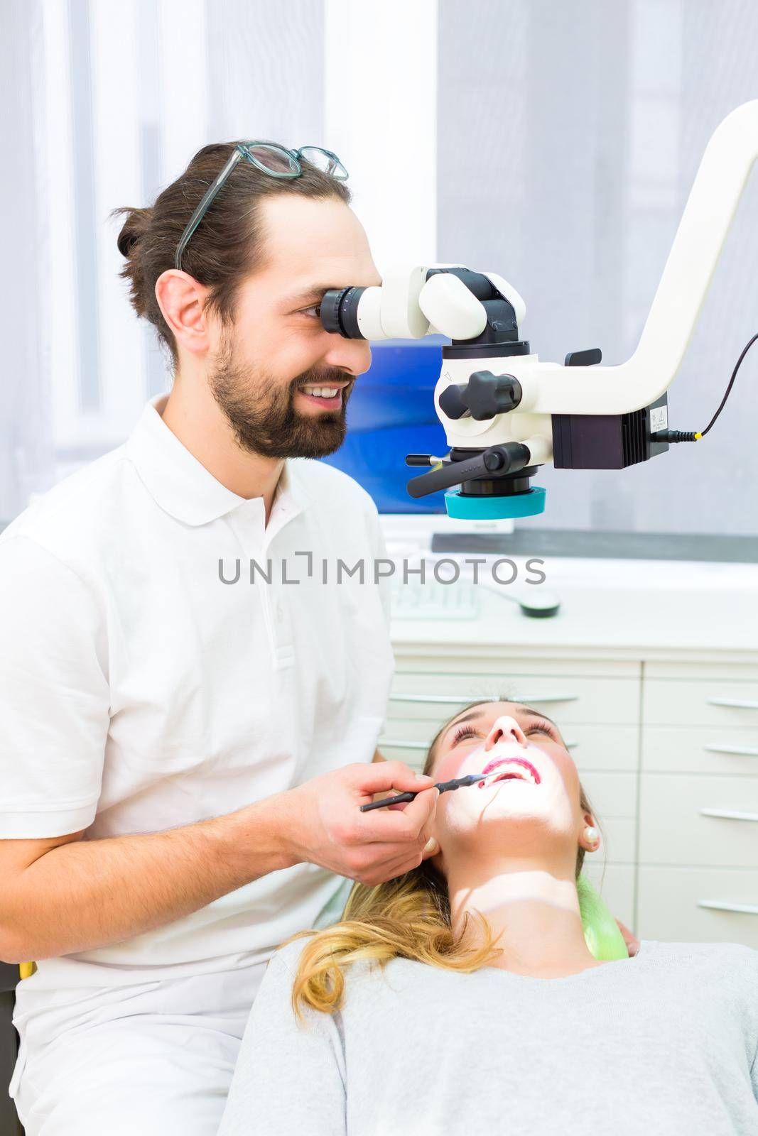 Dentist using microscope to check teeth of patient by Kzenon