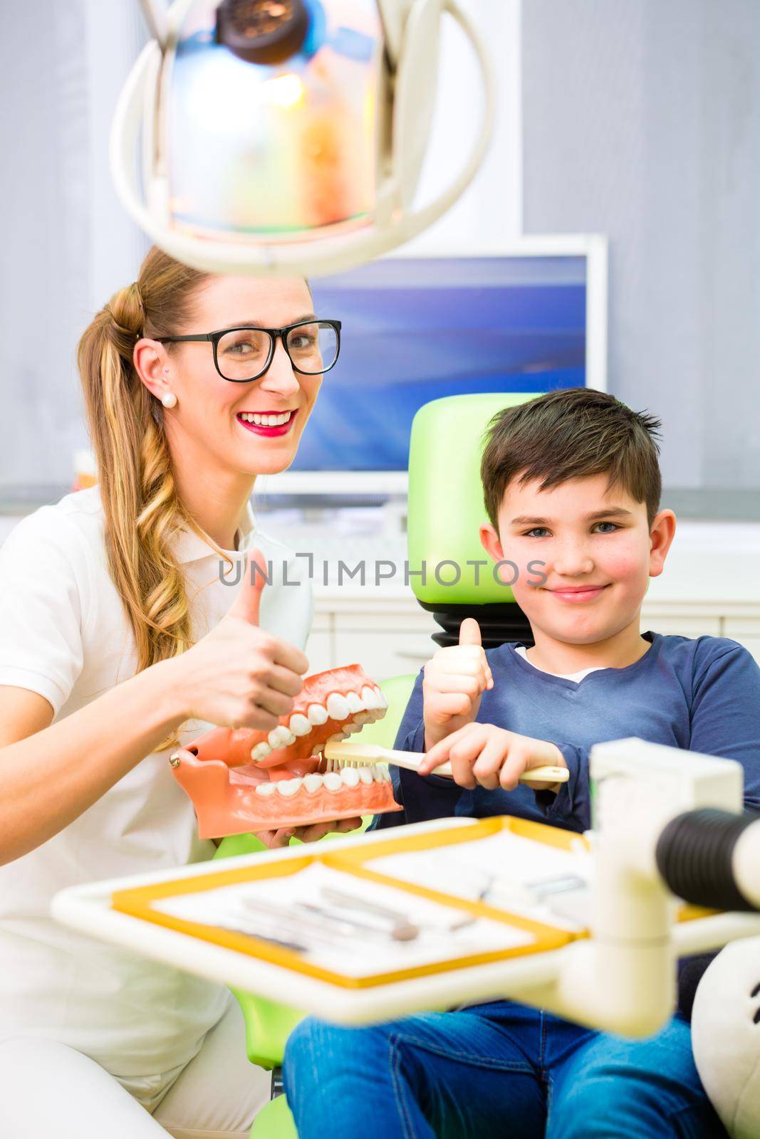 Female dentist explaining boy cleaning tooth with toothbrush on model