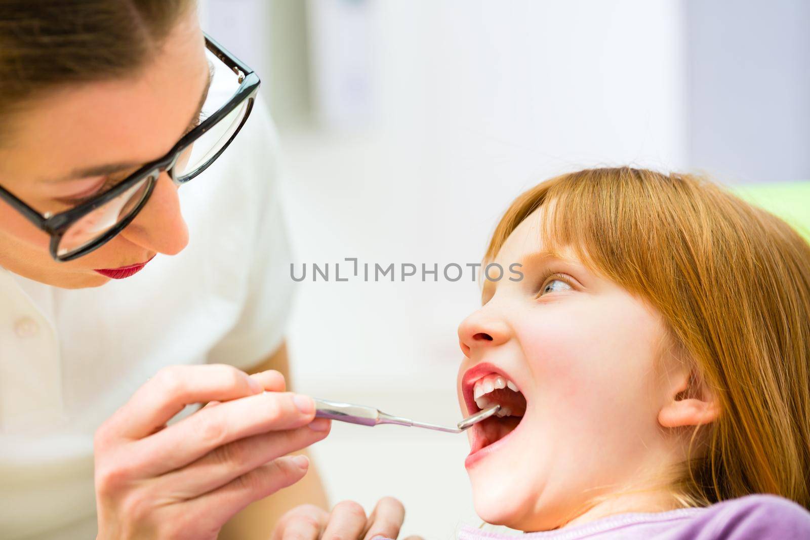 Dentist practicing with child in dental surgery by Kzenon