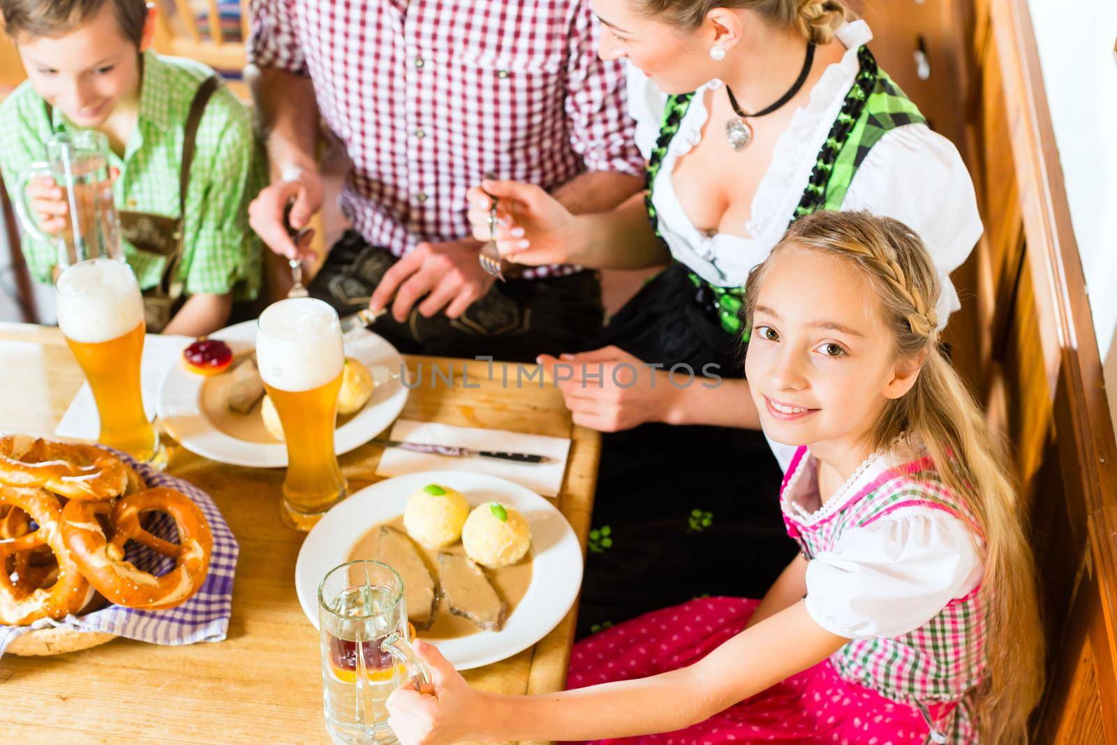 Bavarian girl wearing dirndl and eating with family in traditional restaurant