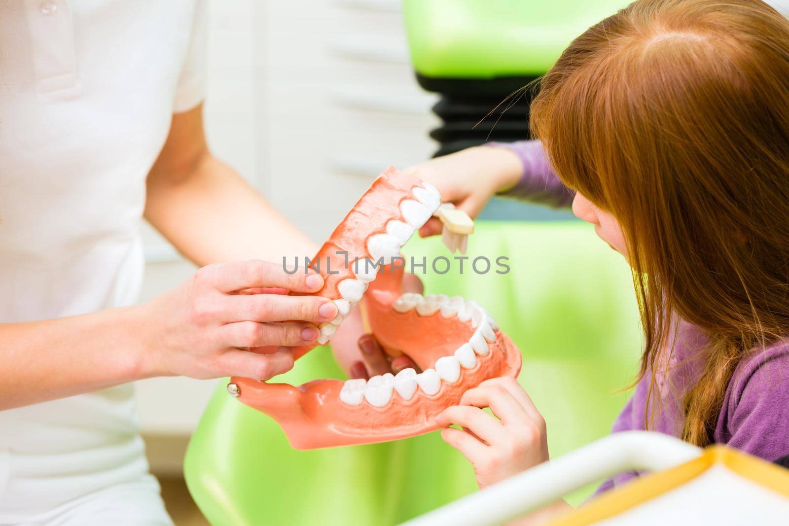 Dentist explaining girl cleaning tooth by Kzenon